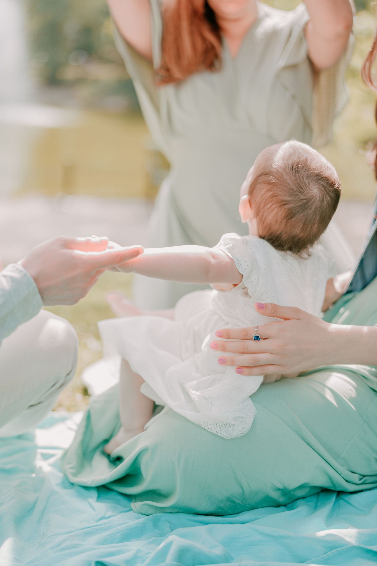 Un bébé vêtu d’une tenue blanche tend la main, installé sur des couvertures turquoise dans une ambiance douce et onirique.