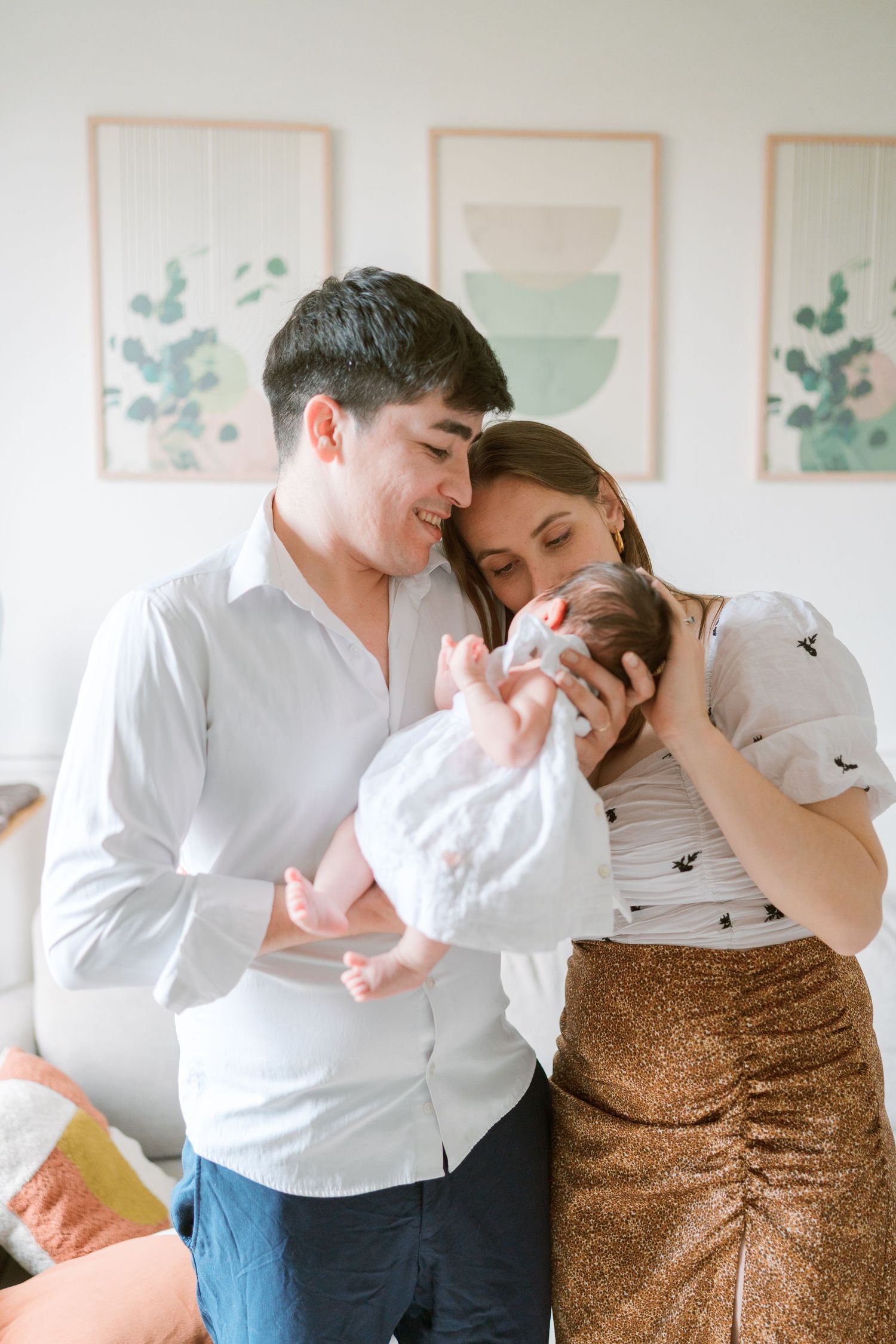 Un couple partage des instants intimes dans une pièce à la lumière douce, avec des œuvres encadrées accrochées au mur derrière eux.
