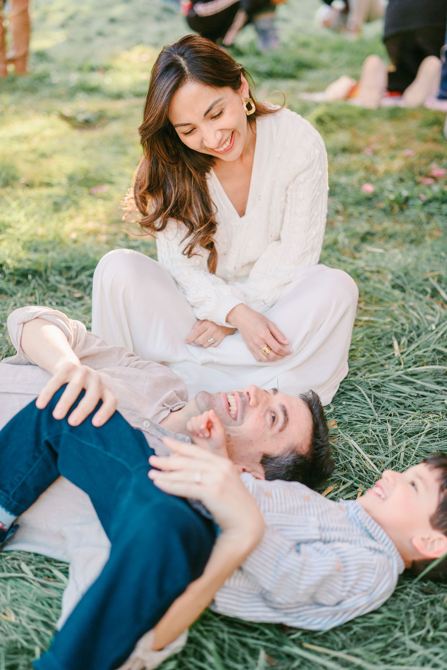 Un moment familial paisible capturé en extérieur, avec des personnes allongées dans l’herbe, habillées de manière décontractée.
