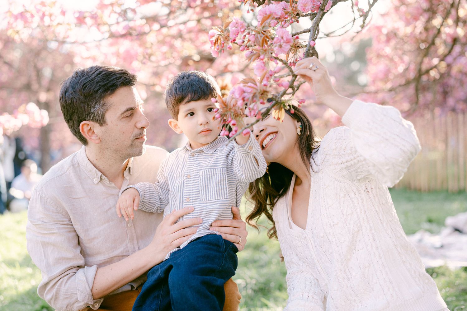 A family shares a joyful moment together under blooming pink cherry blossom trees in a spring garden setting.