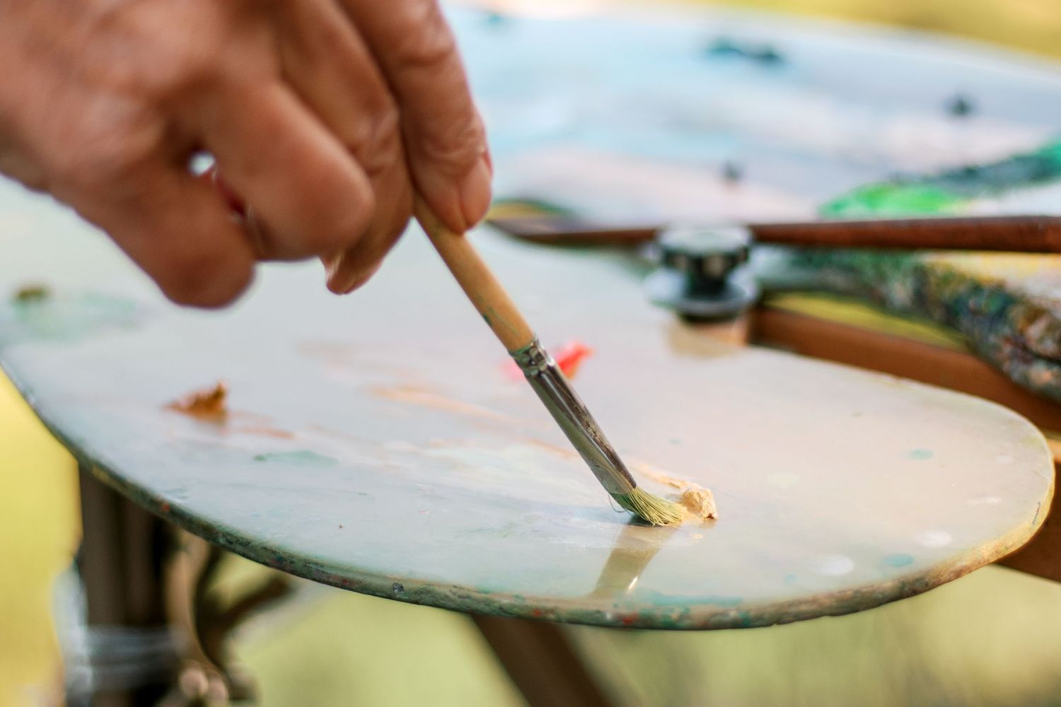 Artist mixing paint on a palette with a fine brush outdoors in natural light.