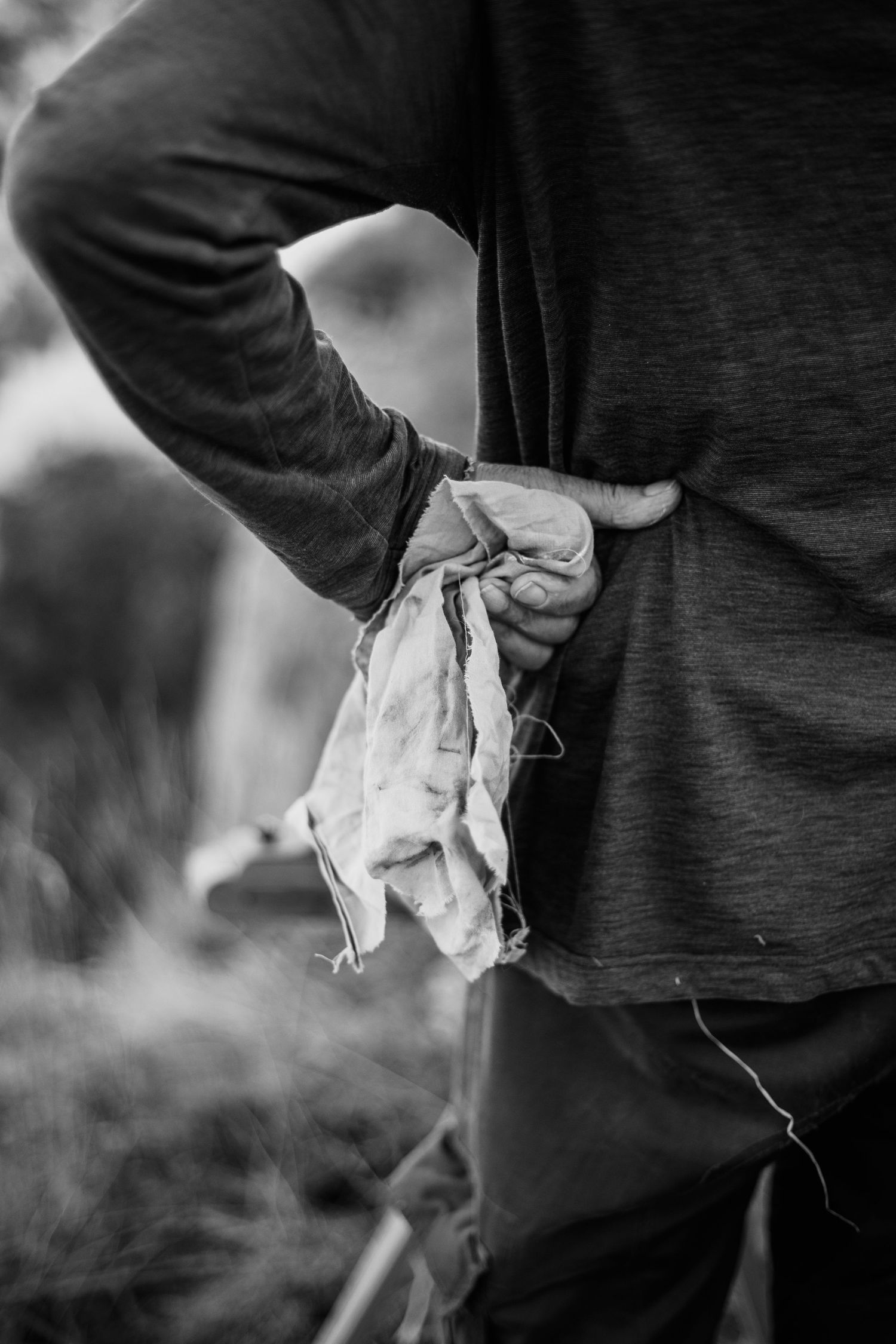 Black and white photo of a person holding a worn cloth rag behind their back outdoors.
