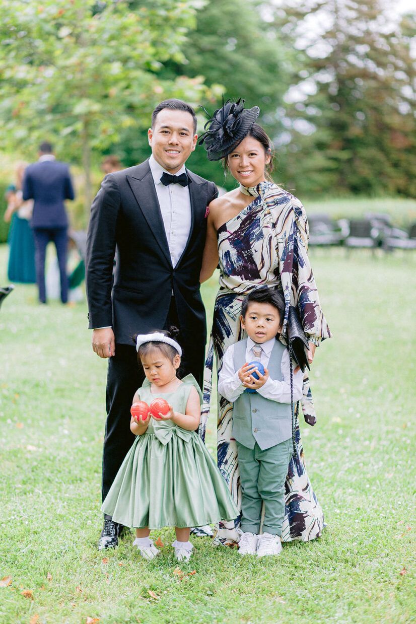 Family of four poses outdoors at a wedding, parents in formal attire with two young children dressed in sage green and gray.