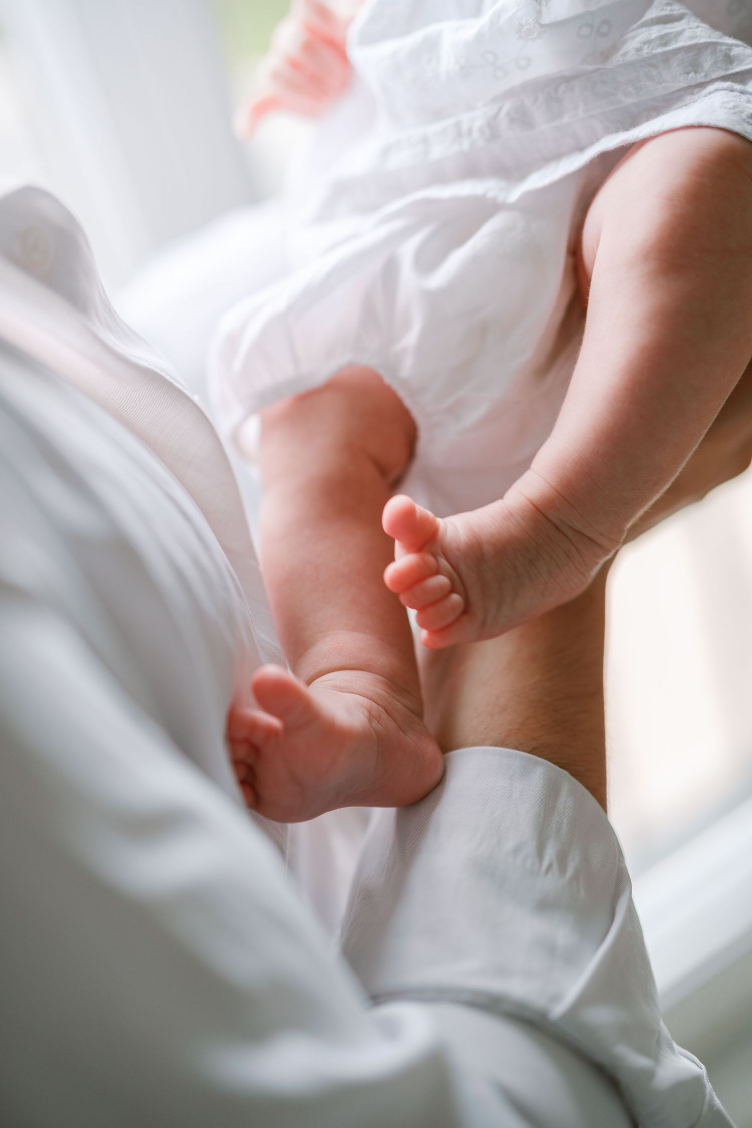 Gros plan de petits pieds de bébé reposant sur une literie blanche et douce, à la lumière naturelle.