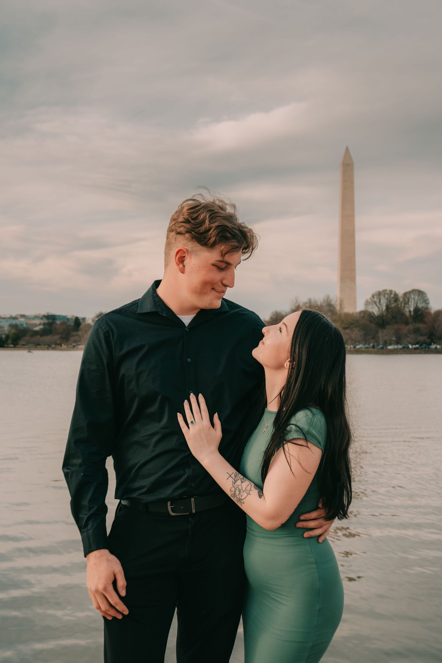 A romantic couple embraces near the Washington Monument by the Tidal Basin in Washington DC at dusk.