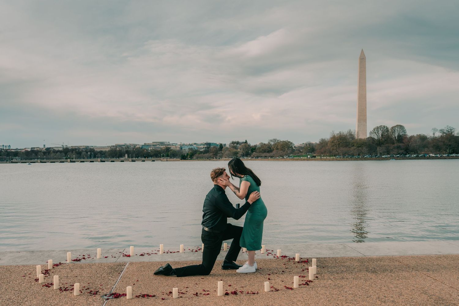 A couple shares a romantic moment by the Tidal Basin with the Washington Monument and glowing candles along the waterfront.