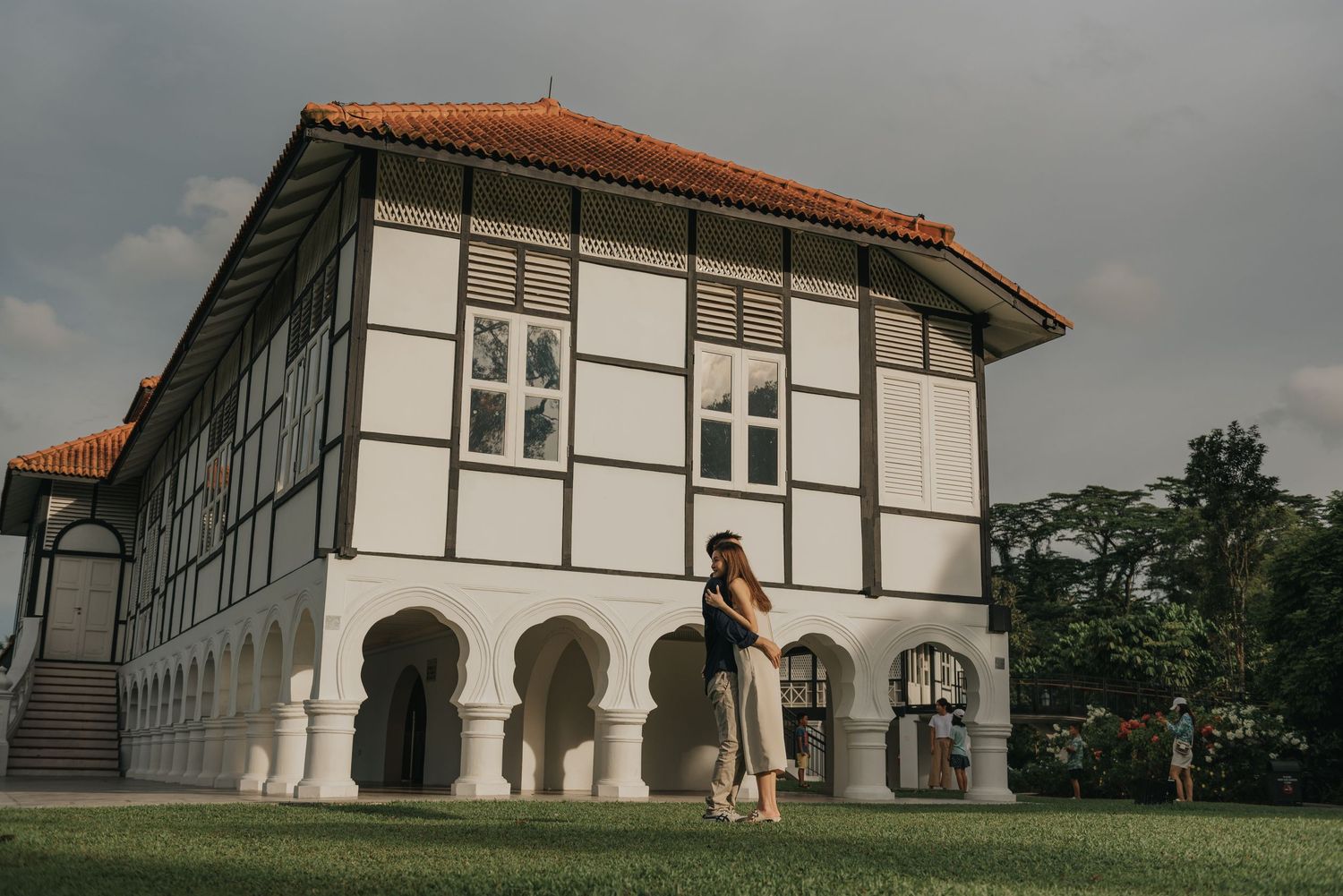 Figure poses elegantly against a white colonial building with distinctive architectural features.