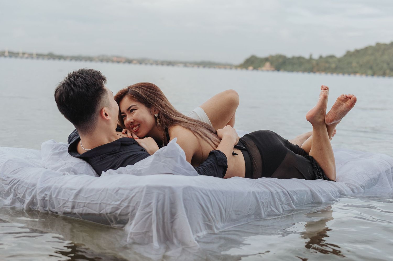 Romantic photoshoot of couple on floating mattress in serene waters.