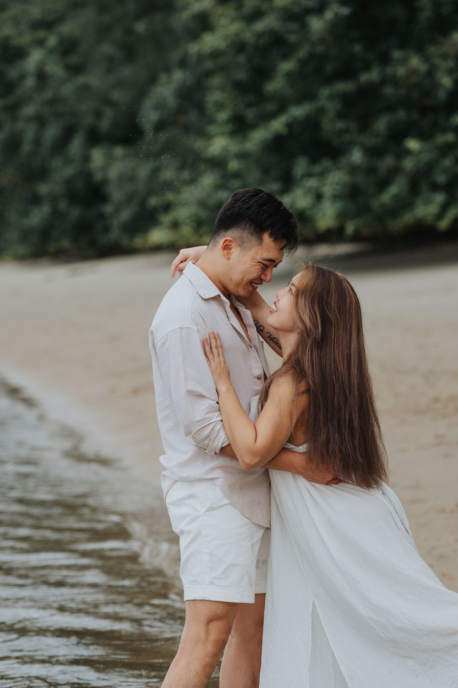 A tender moment between a couple on a scenic beach with waves in the background.