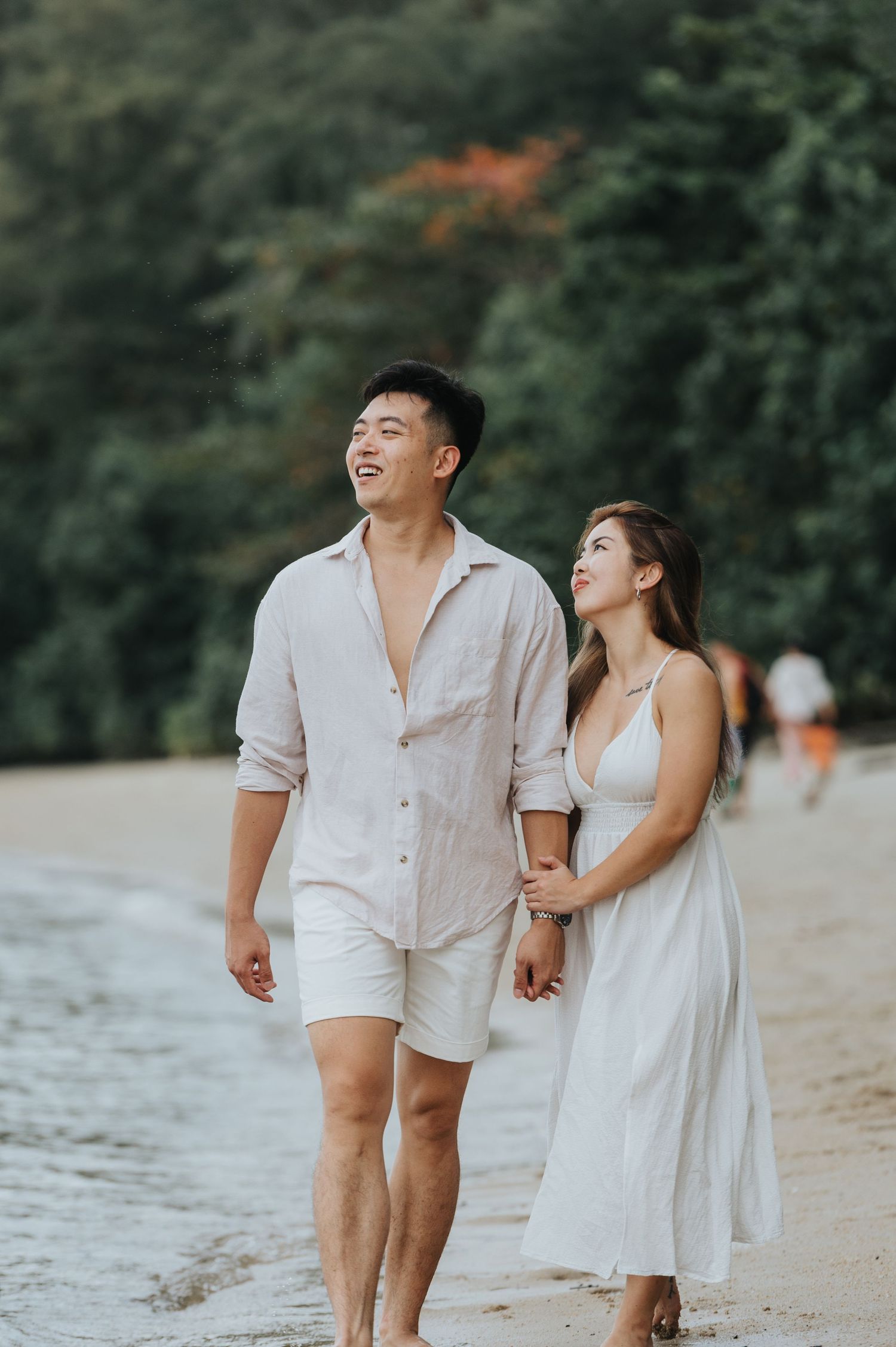 A joyful couple walks along the beach shoreline while sharing a laugh together.
