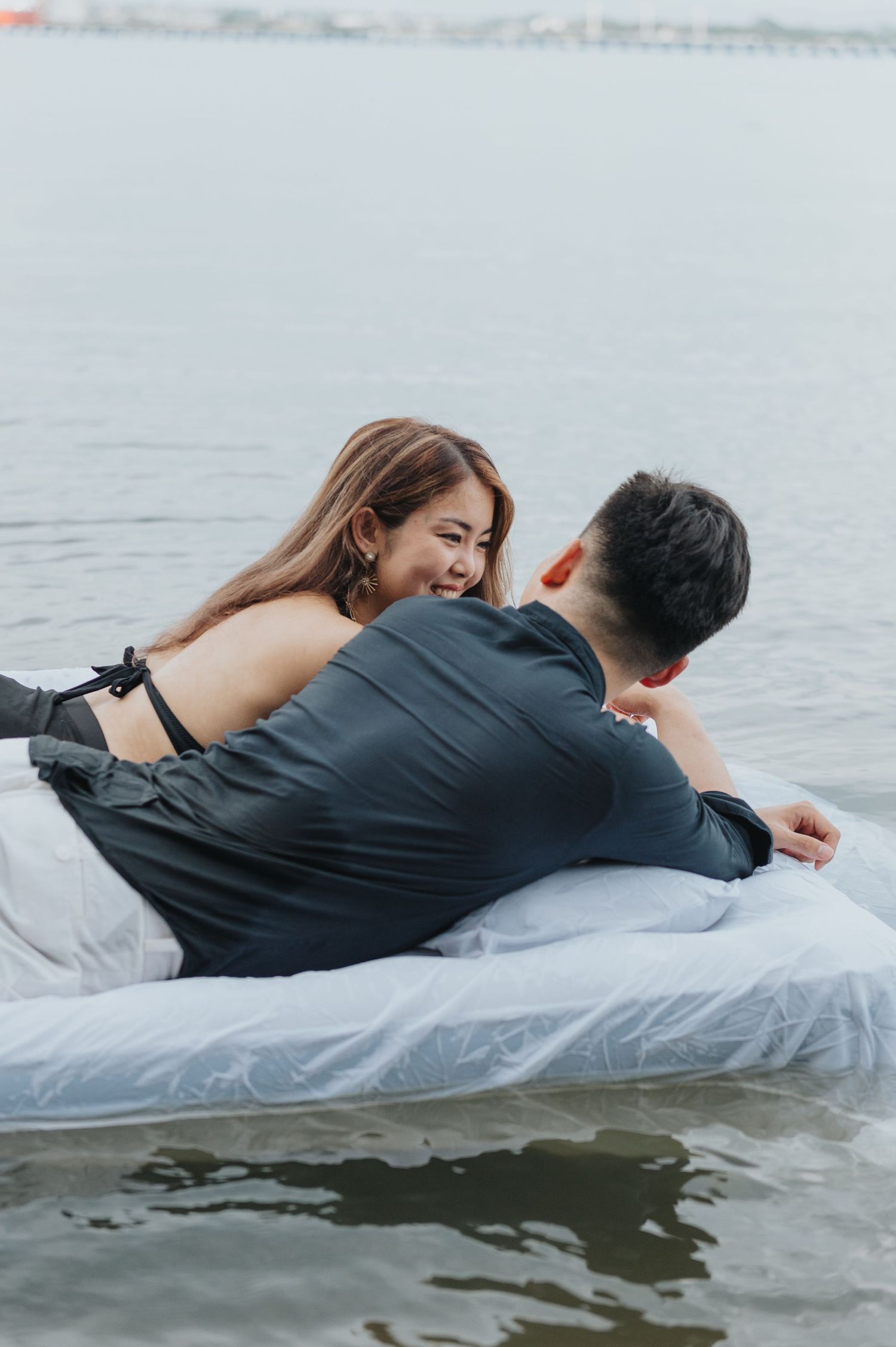 Lovers laying close together on floating white mattress in calm waters.