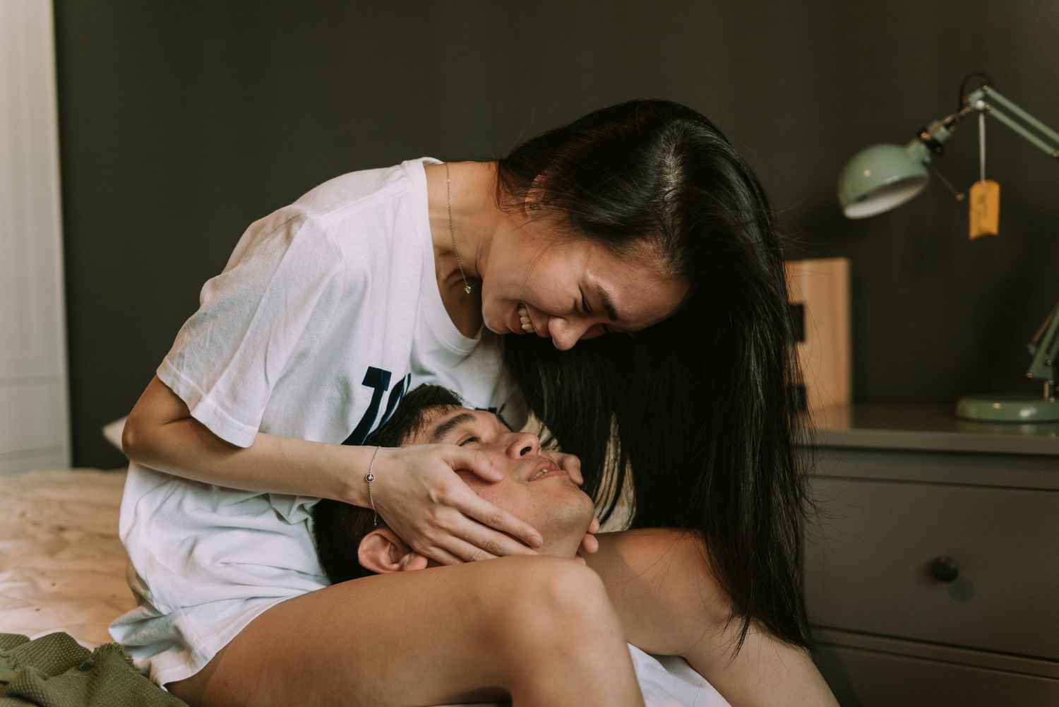 Intimate couple shares a tender moment together on a bed with a desk lamp in the background.