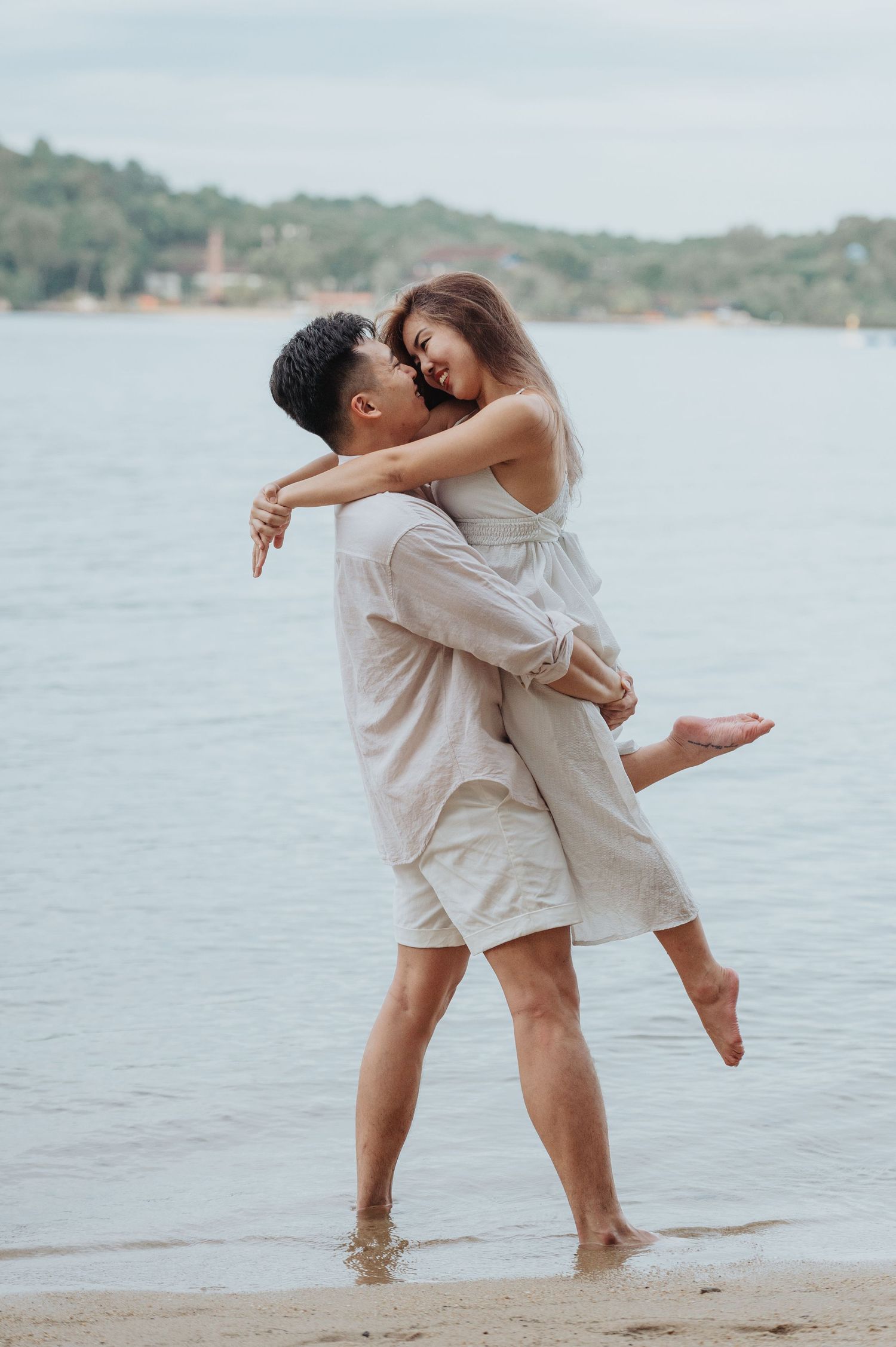 A couple enjoys a playful moment spinning on the beach with one person lifted in the air.