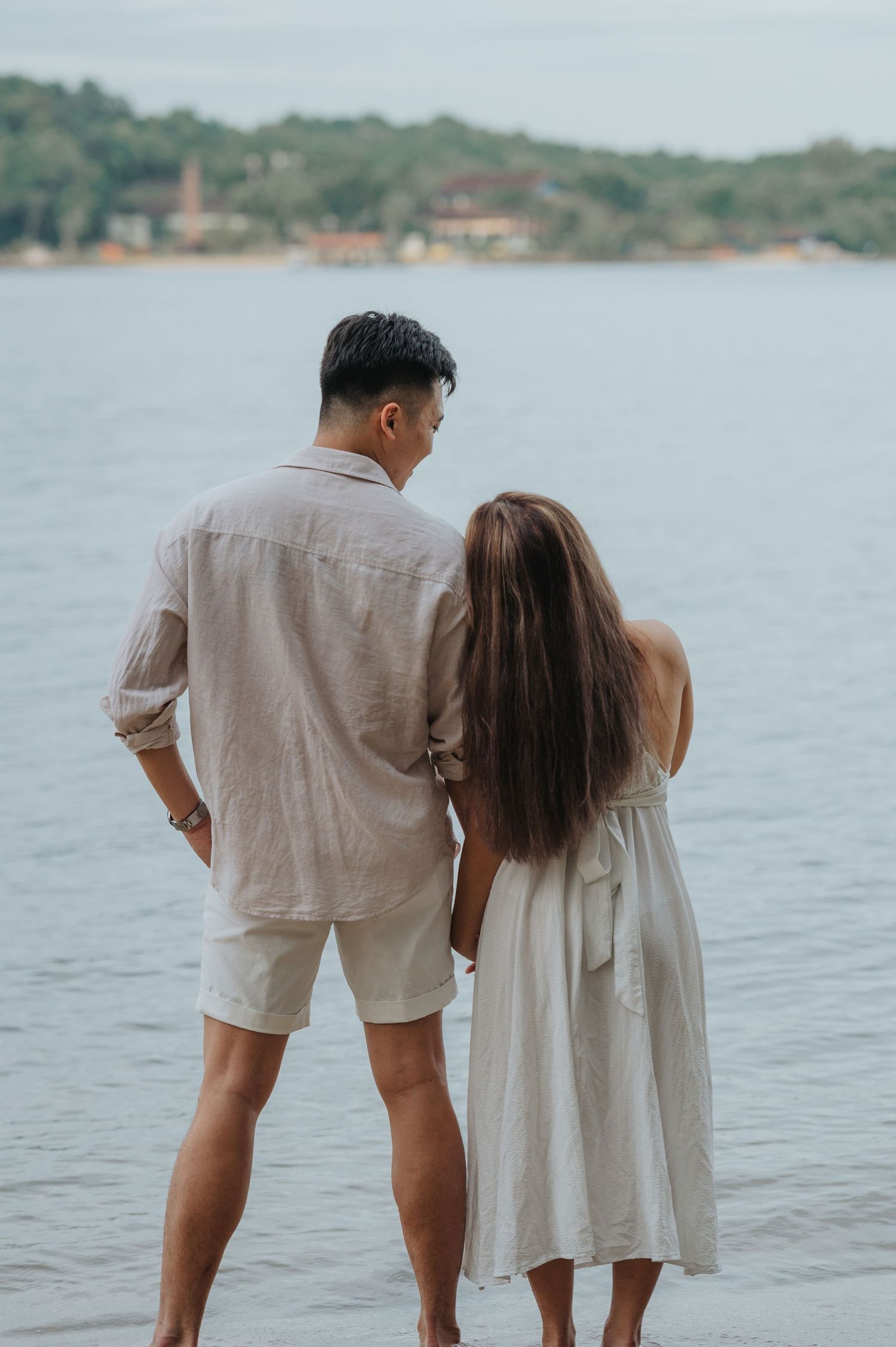 A couple stands together looking out over a scenic bay with distant buildings visible.