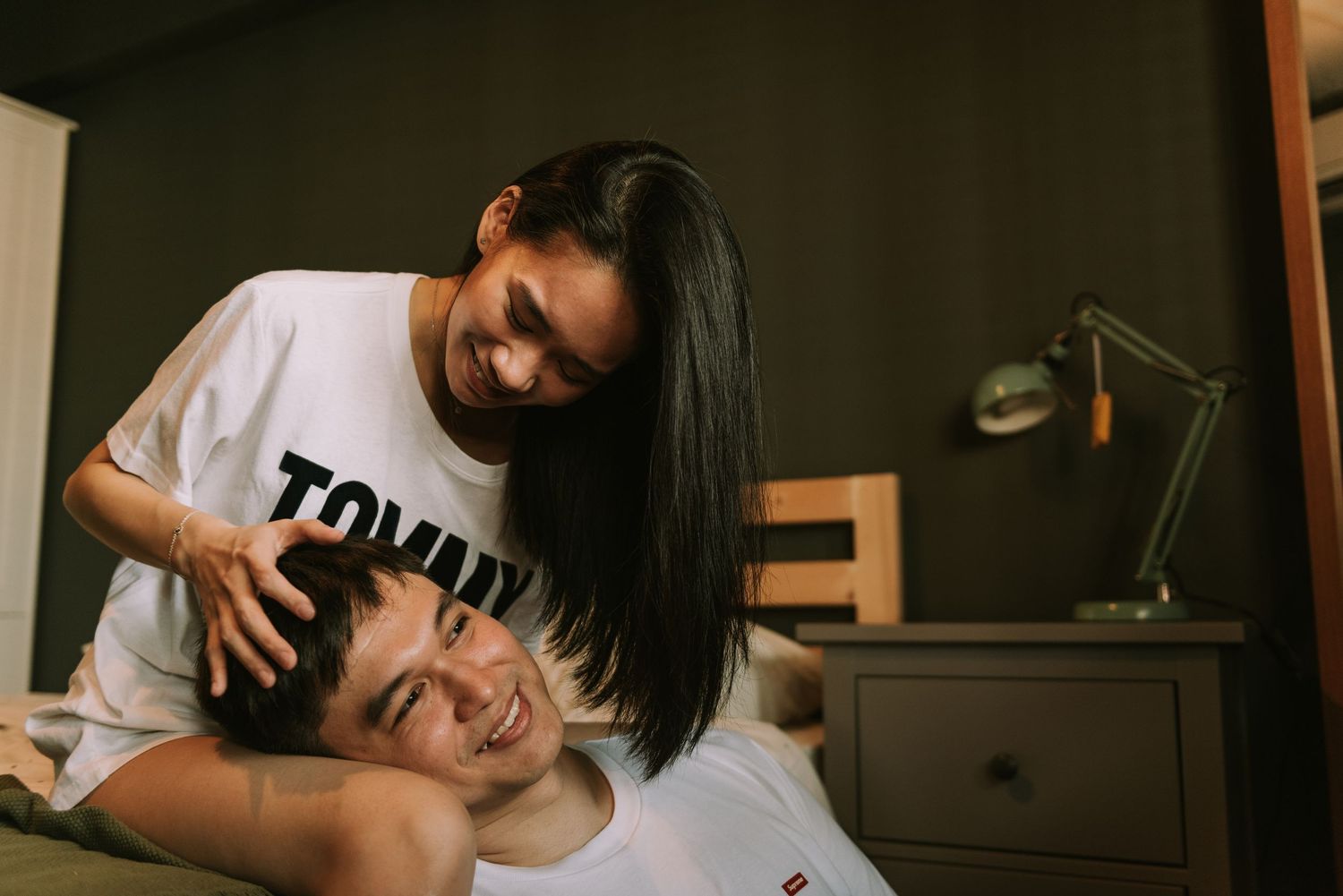 Playful couple in matching white t-shirts sharing laughter during an indoor photoshoot.