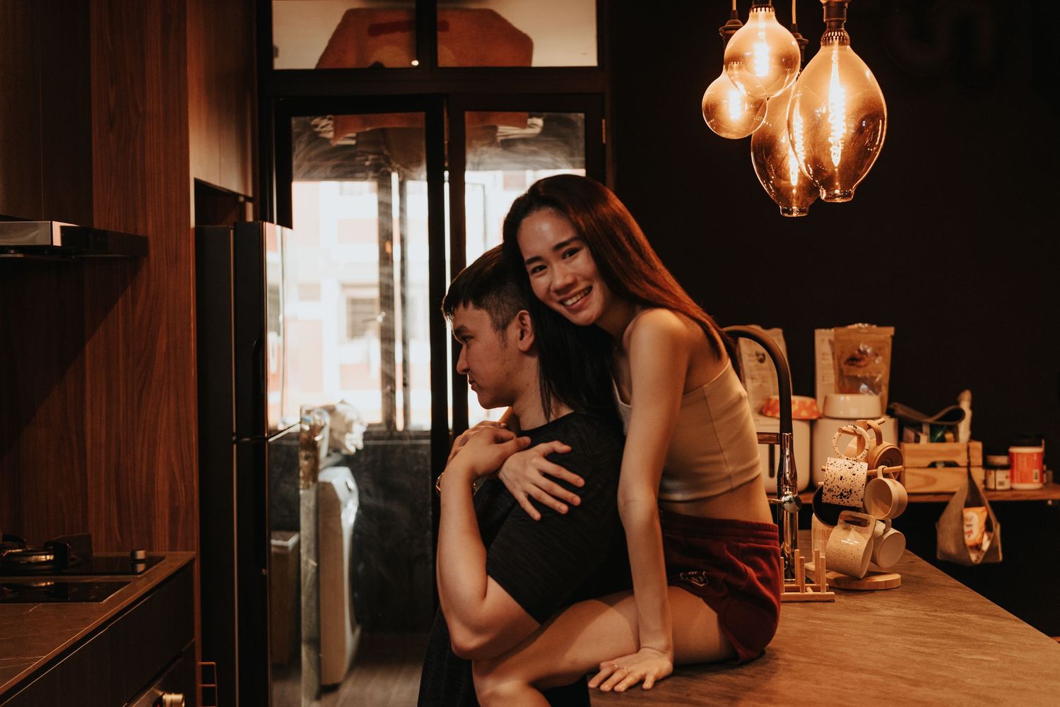 A couple shares an intimate moment in a dimly lit room with vintage pendant lights hanging above.