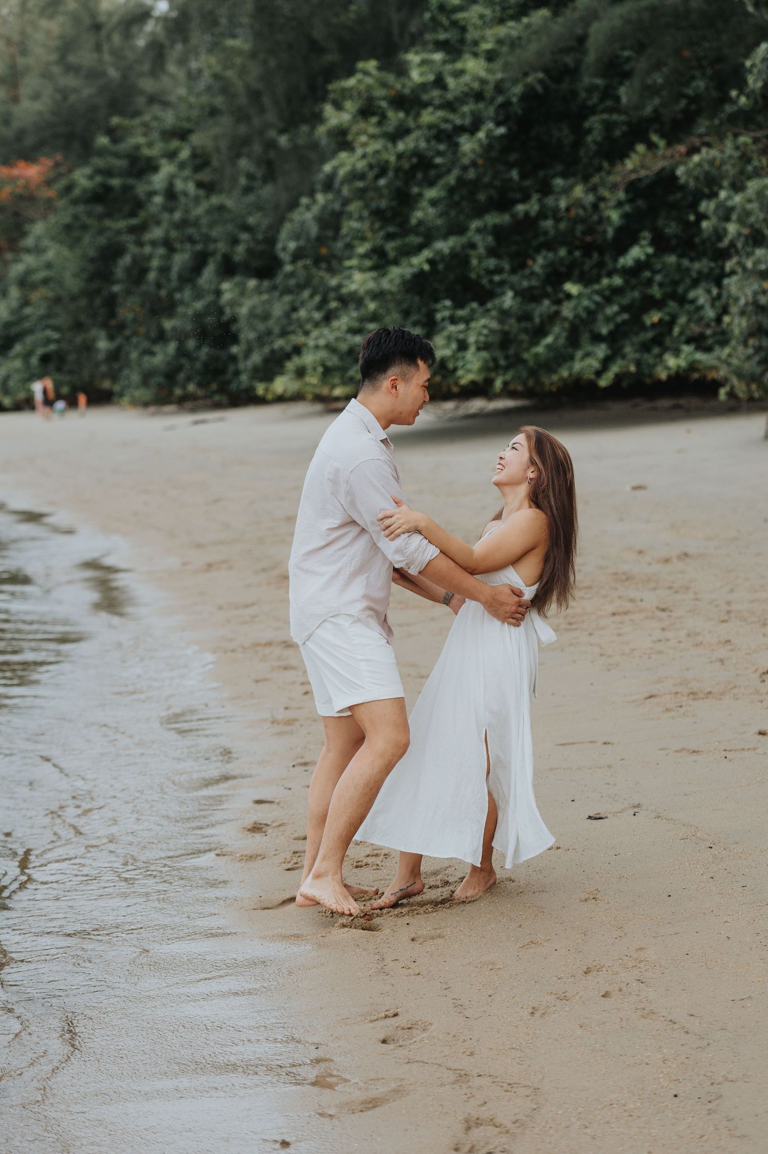 A couple embraces while standing in shallow water at the beach.