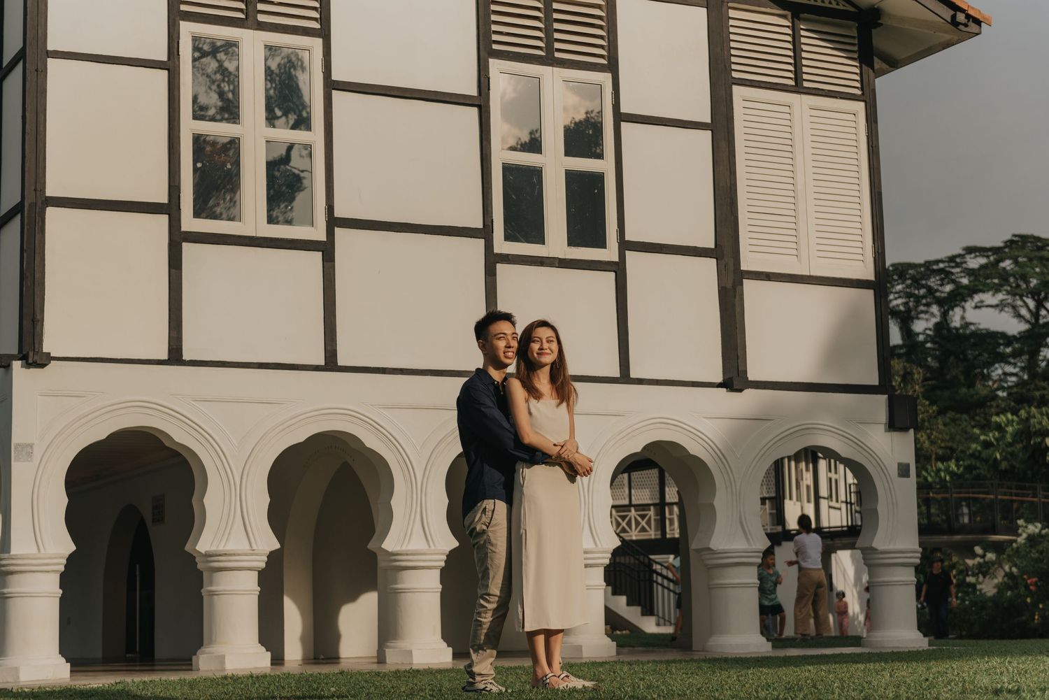 Couple poses beneath white colonial architecture with arched windows and columns.