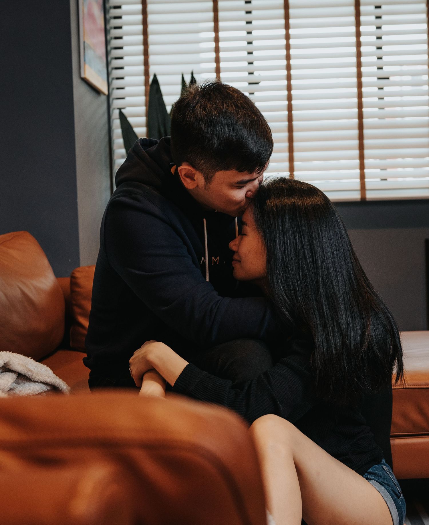 An affectionate couple dressed in black embracing on a tan leather sofa.