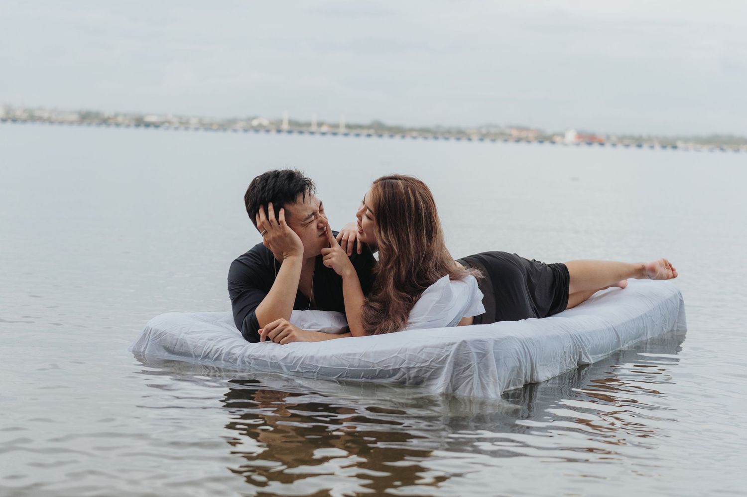 Couple sharing playful moments on a mattress floating in peaceful waters.
