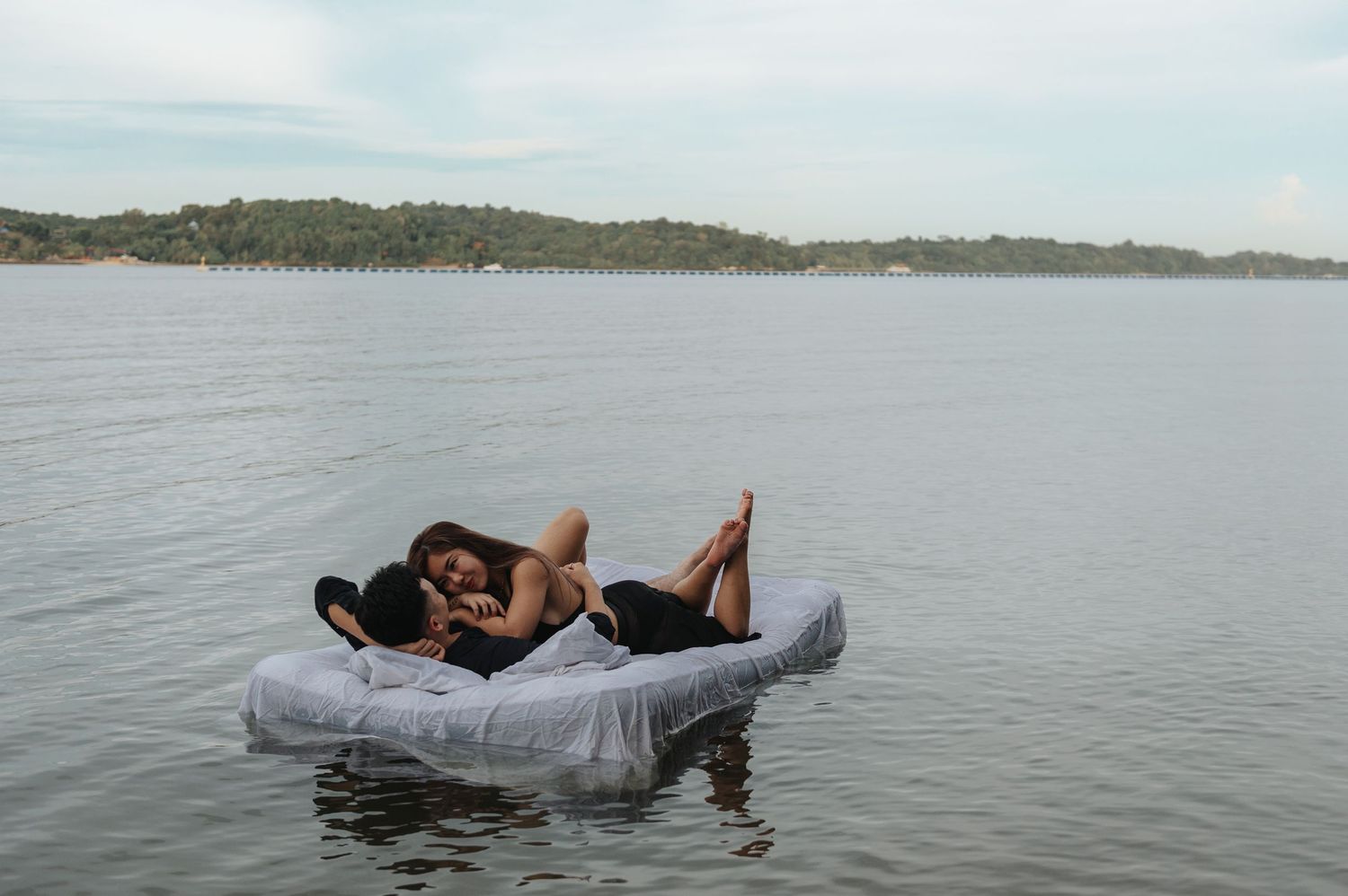 Scenic lakeside photo with couple relaxing on floating mattress near shoreline.