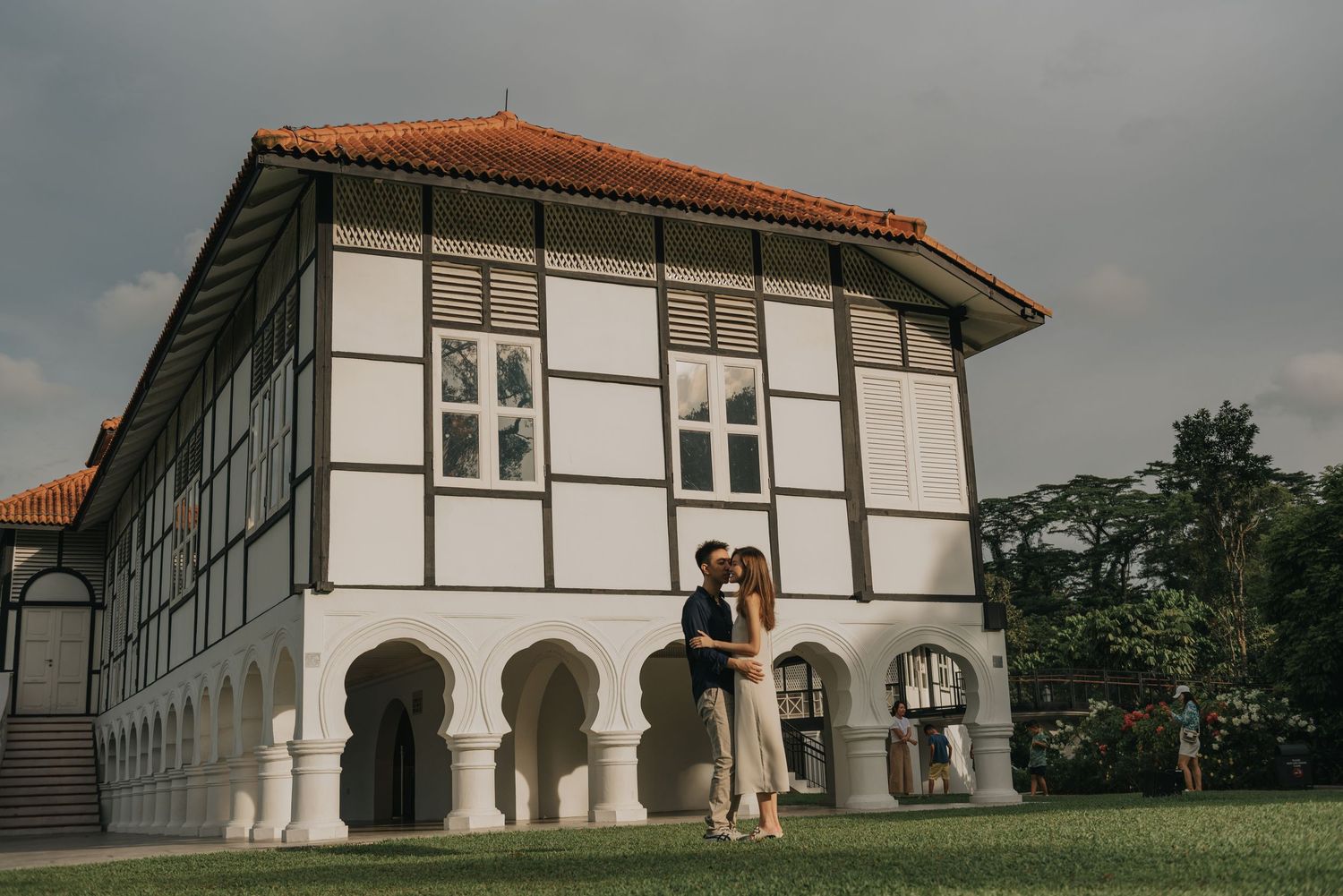 Romantic portrait against a white colonial building with arched windows and terra cotta roof.