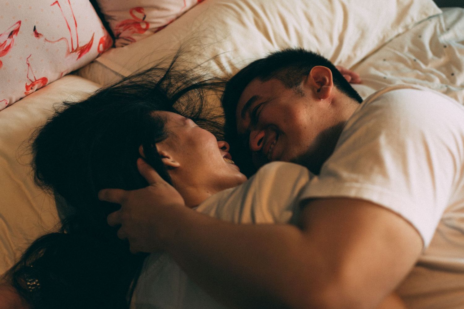 Couple lying close together in dim lighting sharing intimate moment.