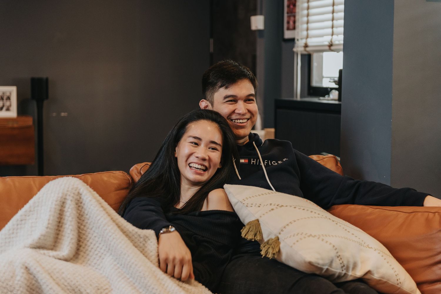 A couple sharing a joyful moment while relaxing on an orange couch with white blankets.