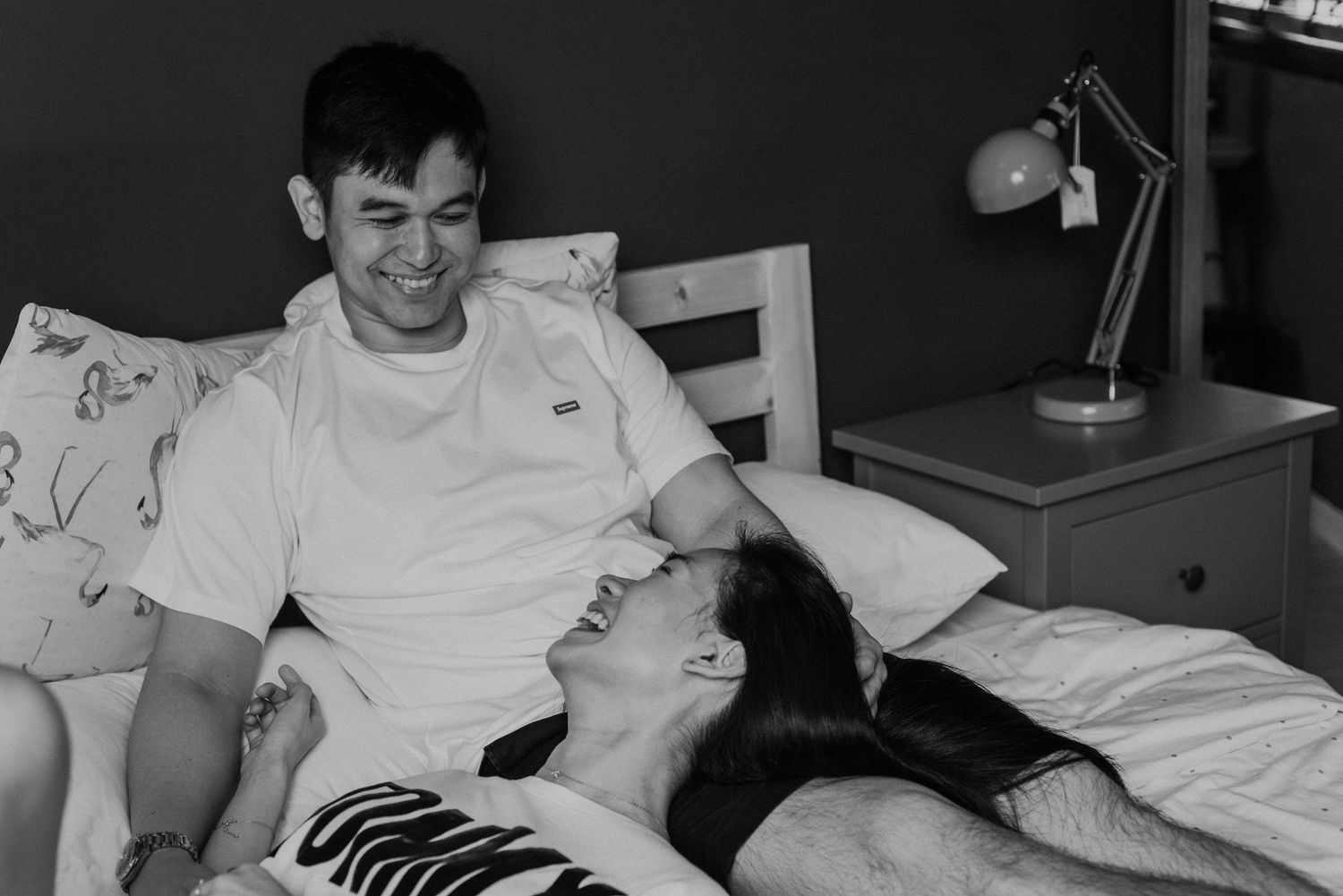 Intimate black and white photo of couple sharing playful moment in bed.