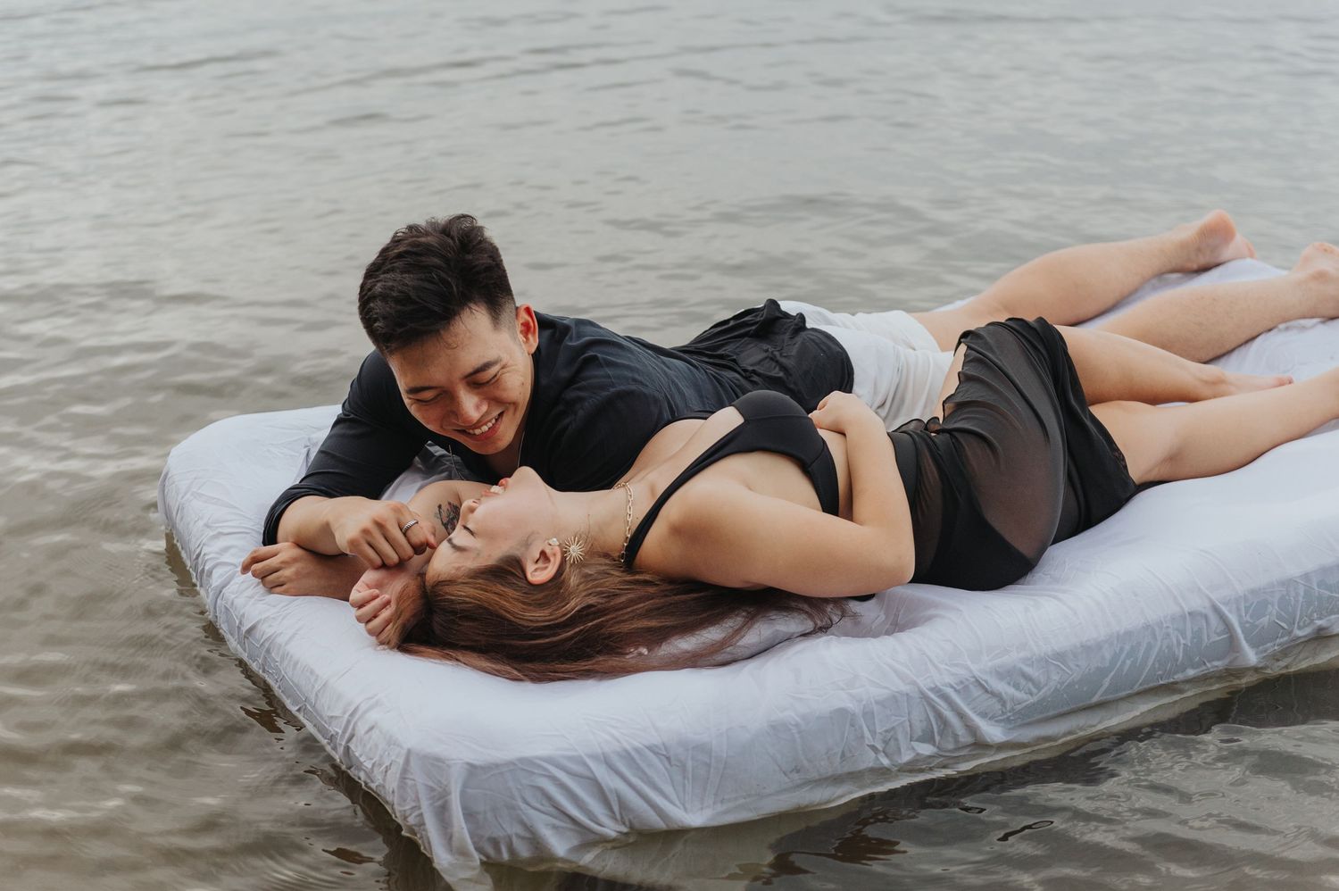 Romantic pair relaxing on floating mattress during dreamy water photoshoot.