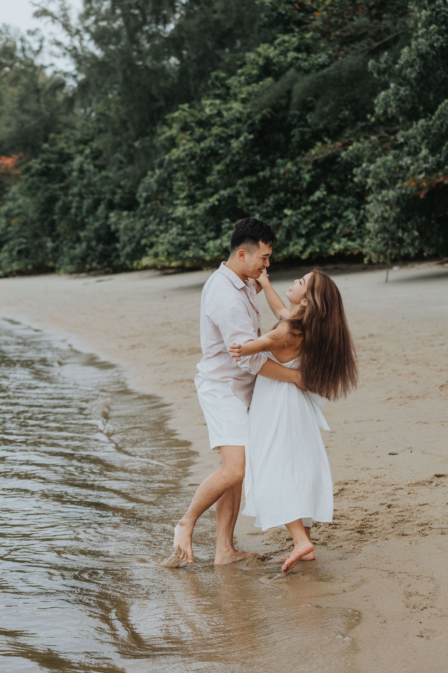 A romantic couple dances together at the water's edge on a scenic beach.