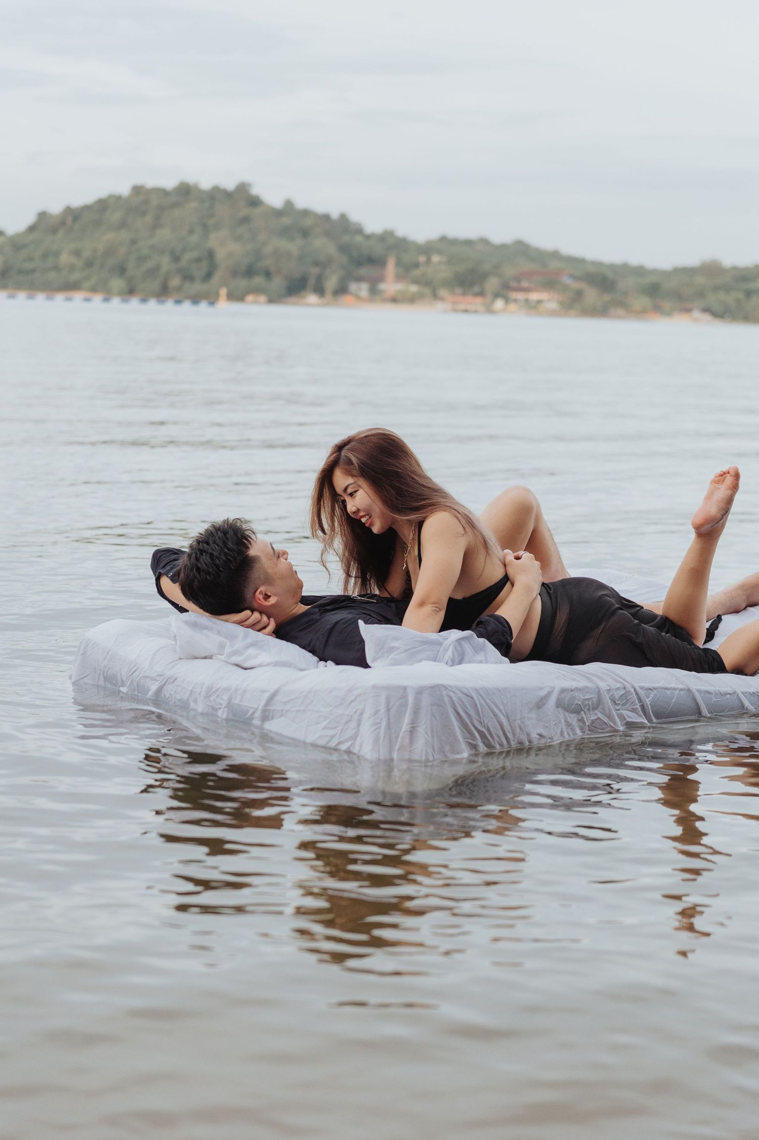 Couple shares tender moment on mattress floating in mountain lake.
