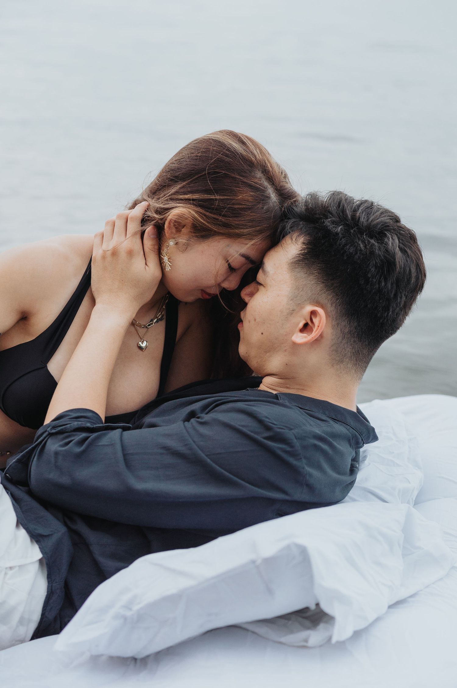 A tender close-up moment between a couple lying on white bedding at the beach.