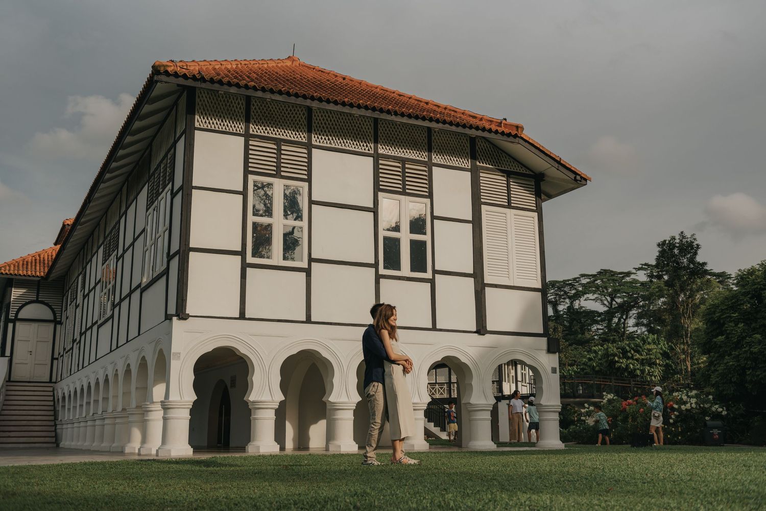 Person stands beside a white colonial building with black timber framing and arched windows.