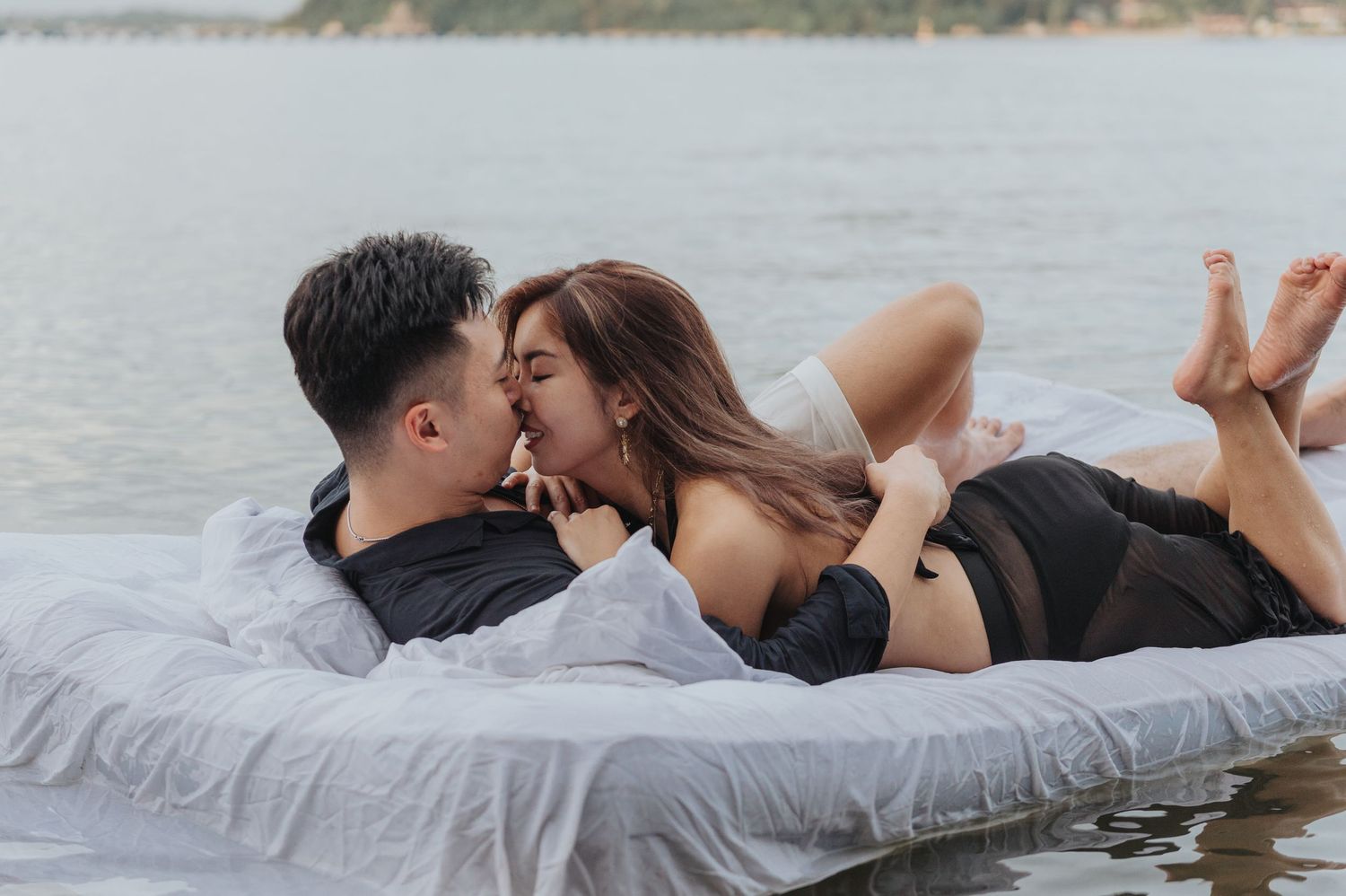 Couple embracing on a mattress floating in calm waters with mountains in the background.