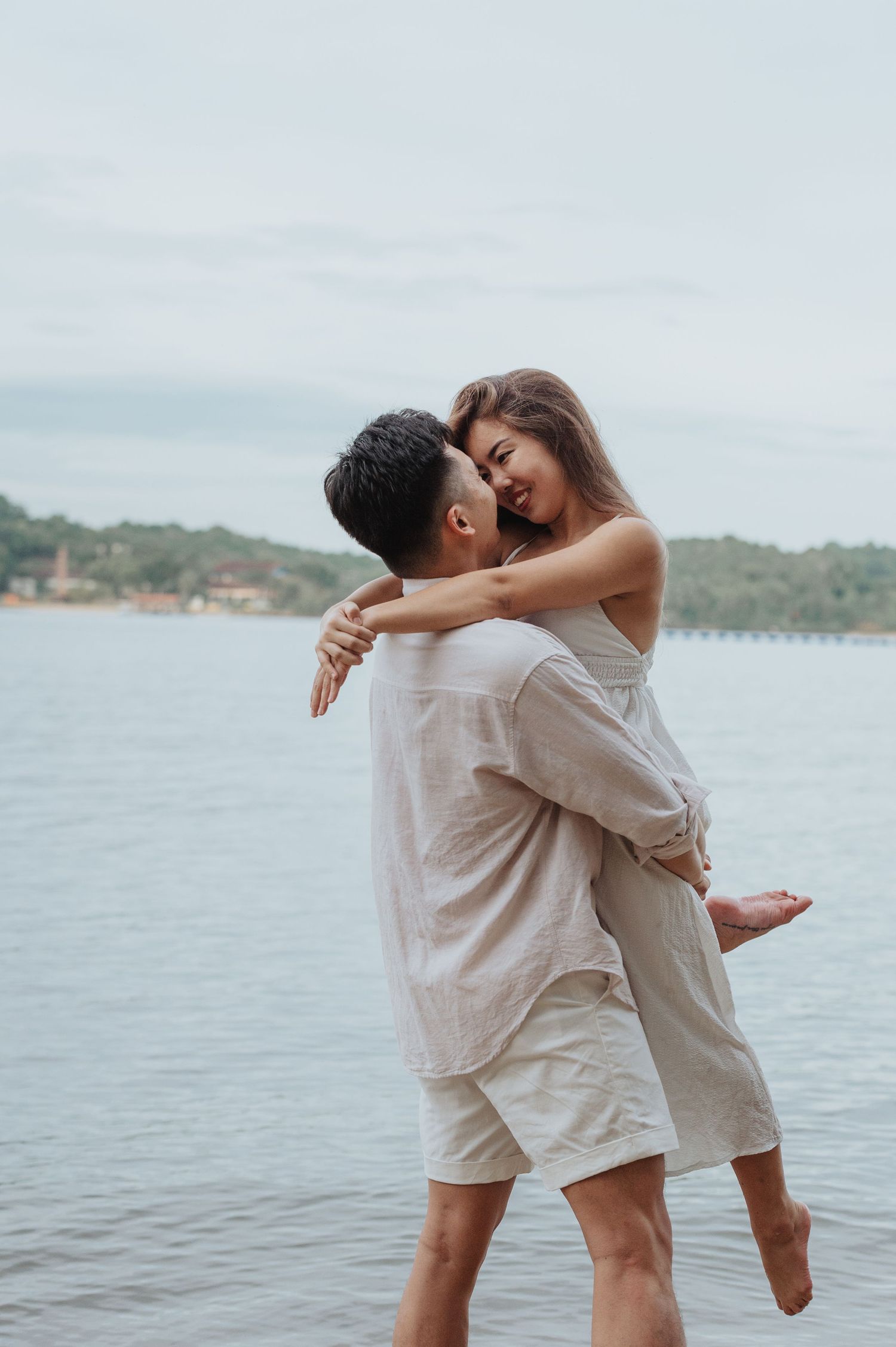 A joyful couple shares a playful embrace on the beach with one person lifted off the ground.