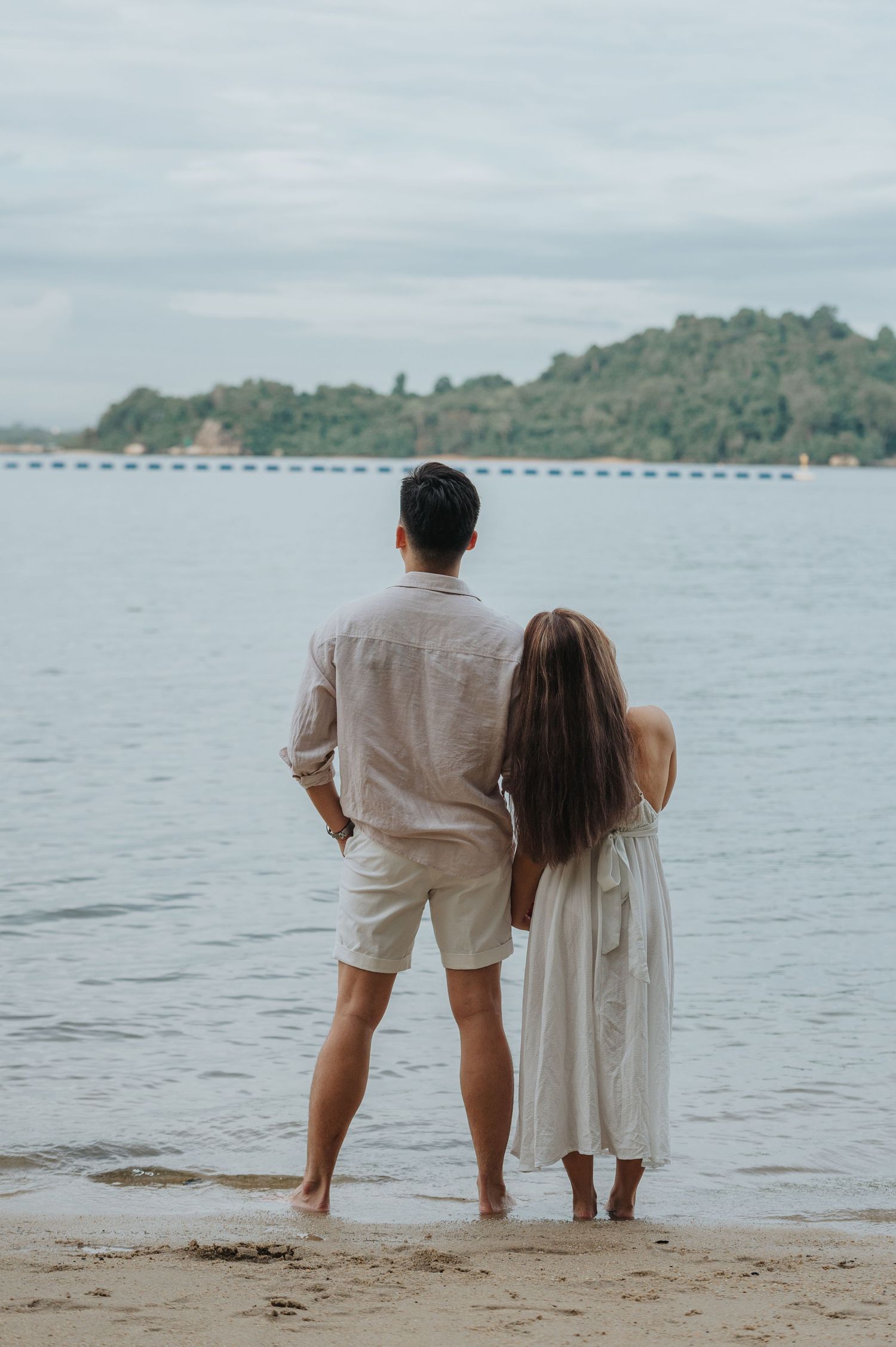A couple stands together looking out at the ocean view.