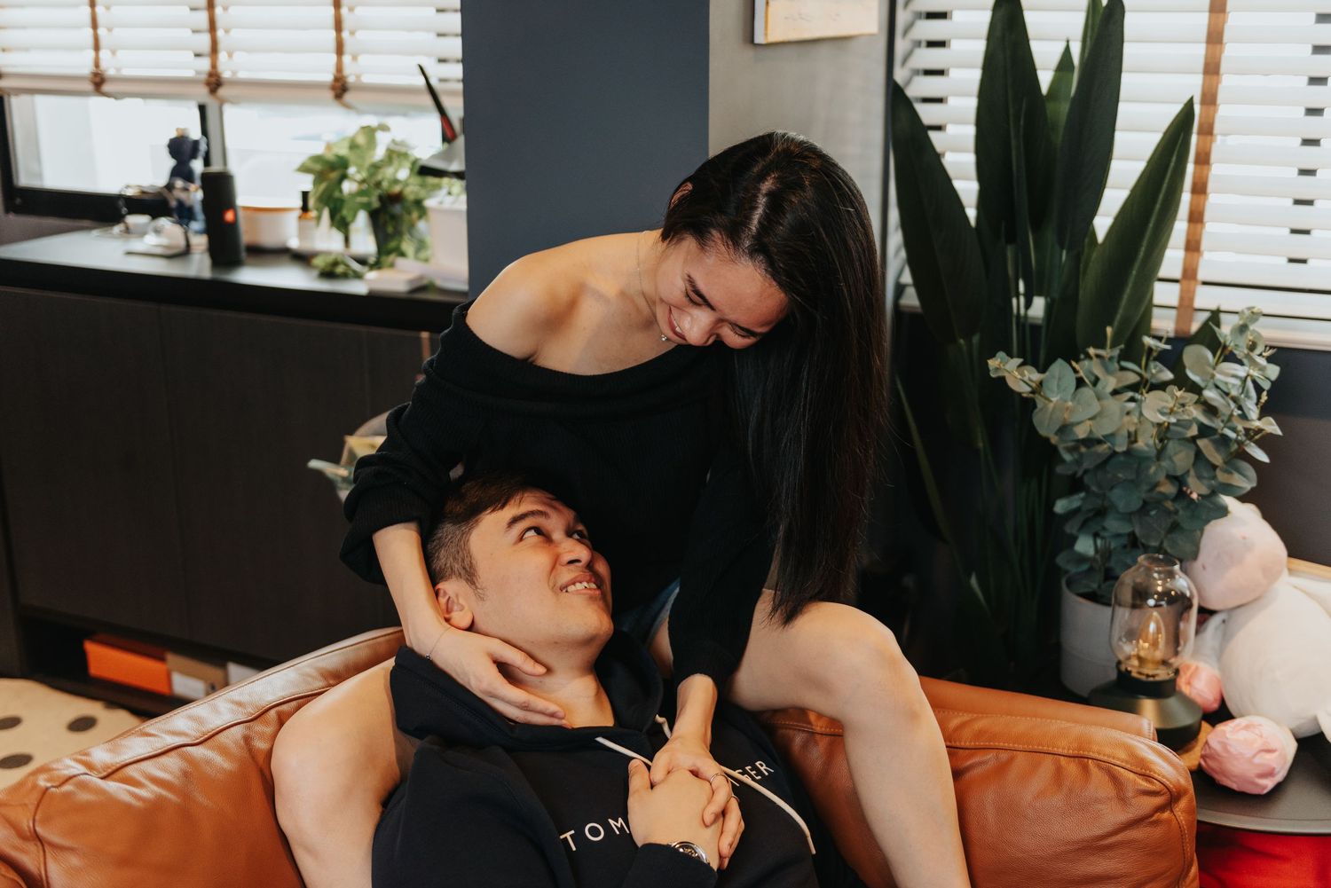 Couple sharing intimate moment on orange couch with decorative plants in background.