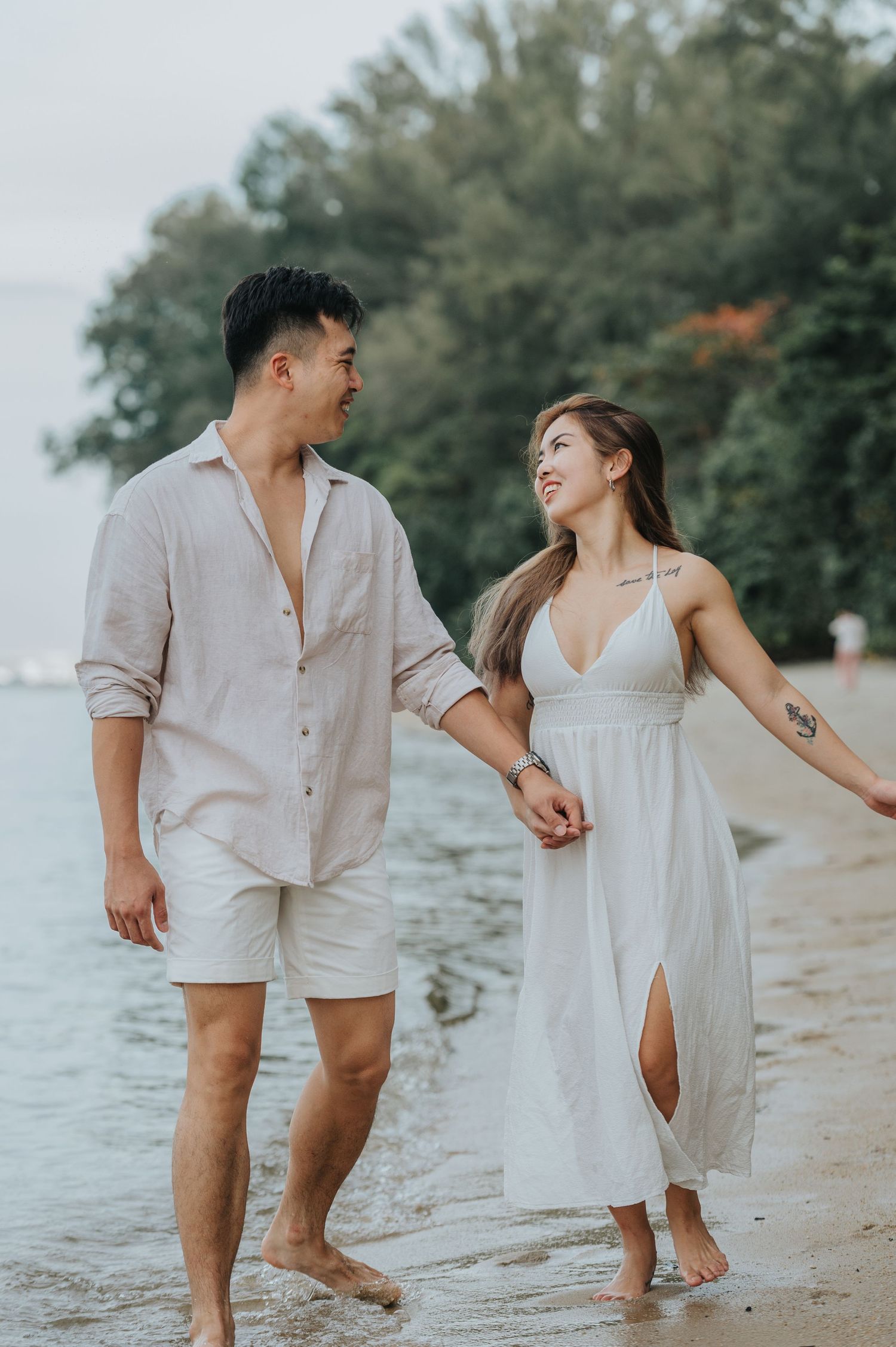 A romantic couple takes a seaside stroll together in coordinated white summer outfits.
