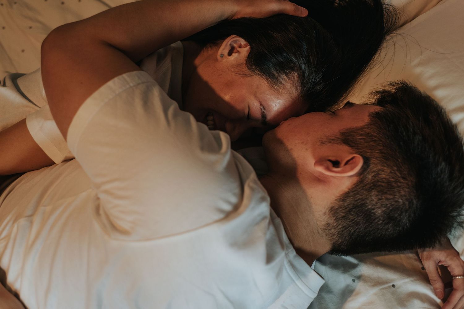 Close up photo of couple resting together on white bedding.