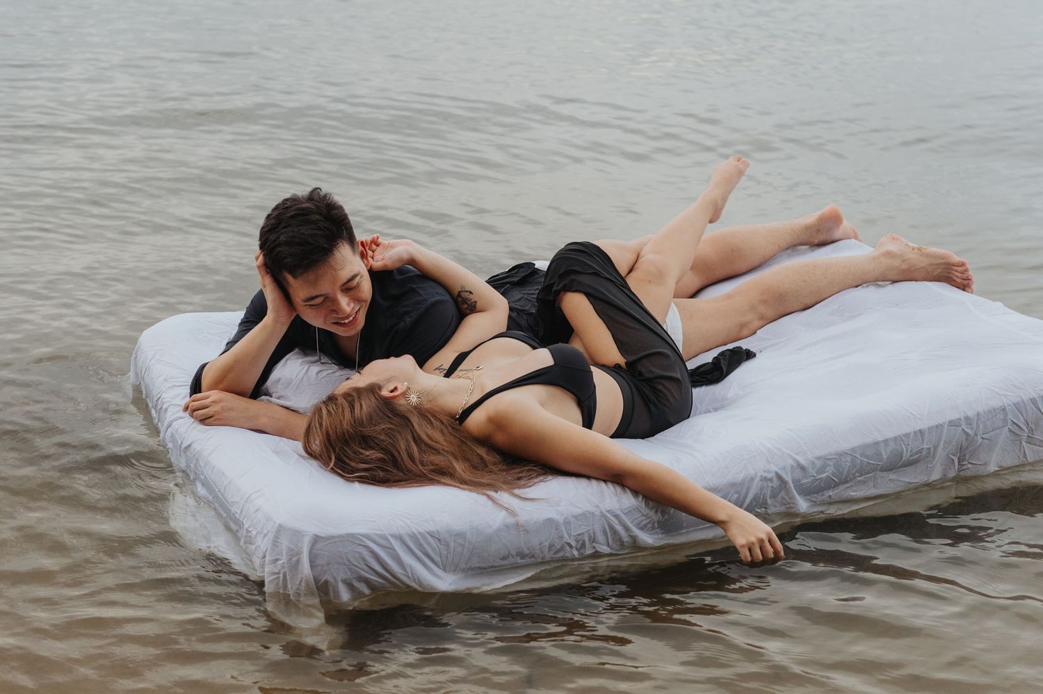 Couple laughing and enjoying intimate moments on mattress floating in water.