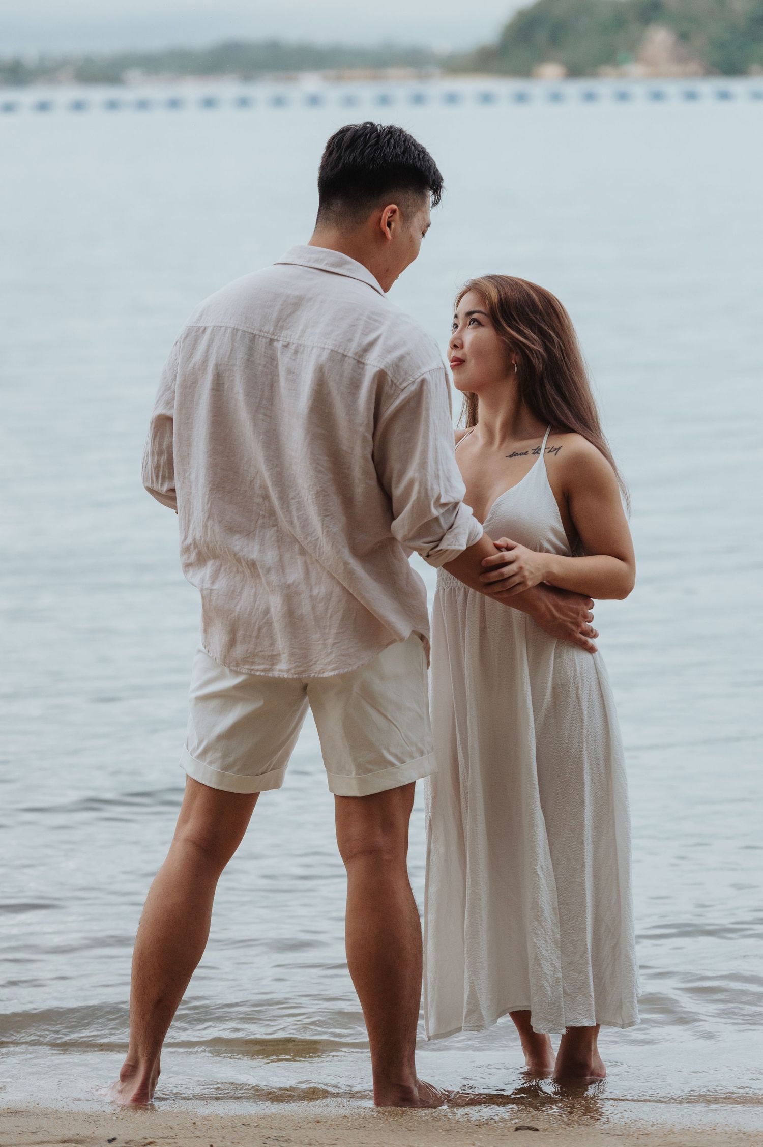 A tender moment between a couple standing in shallow water wearing matching light colored outfits.