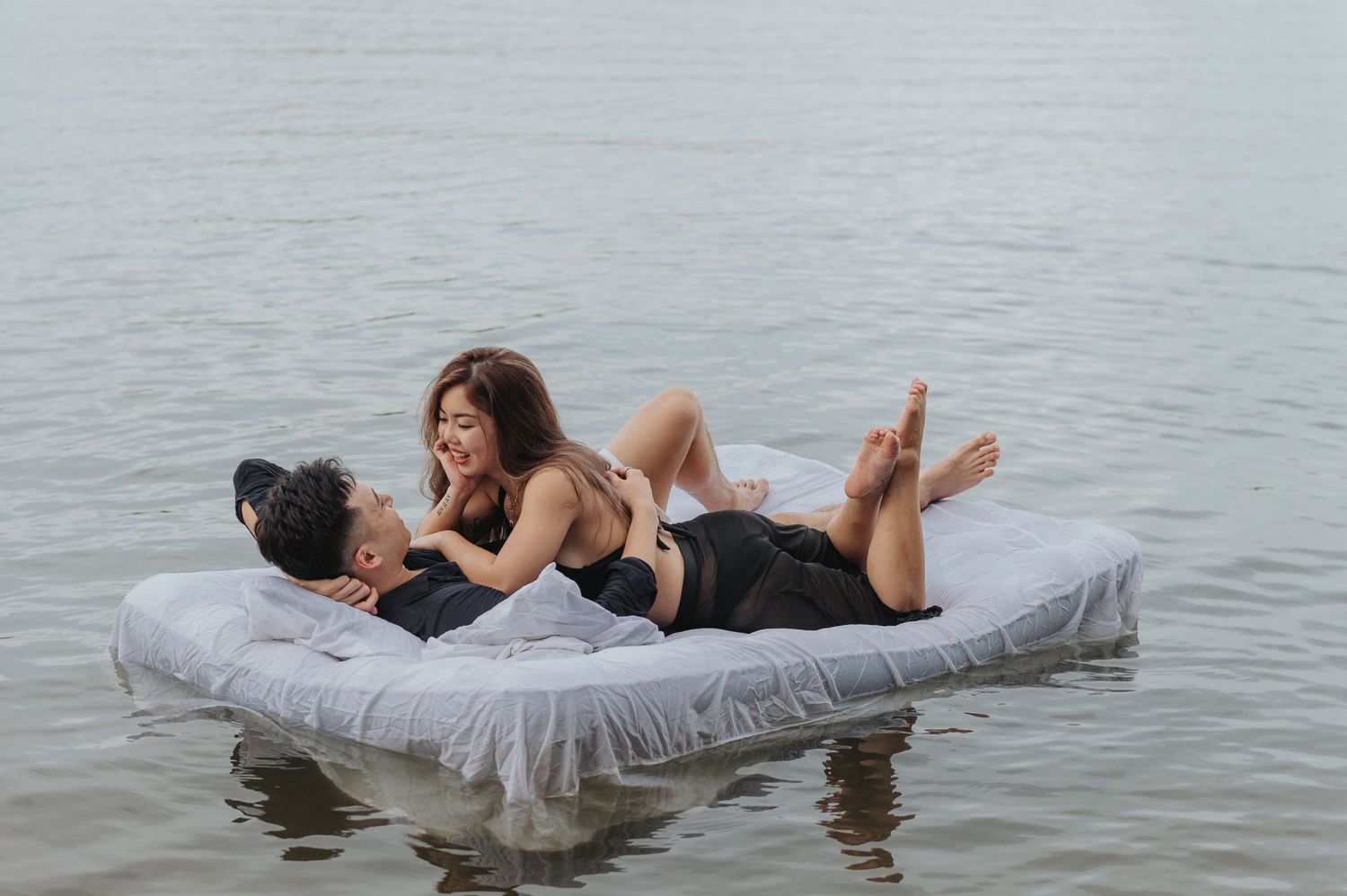 Romantic scene of couple on floating mattress in serene lake waters.