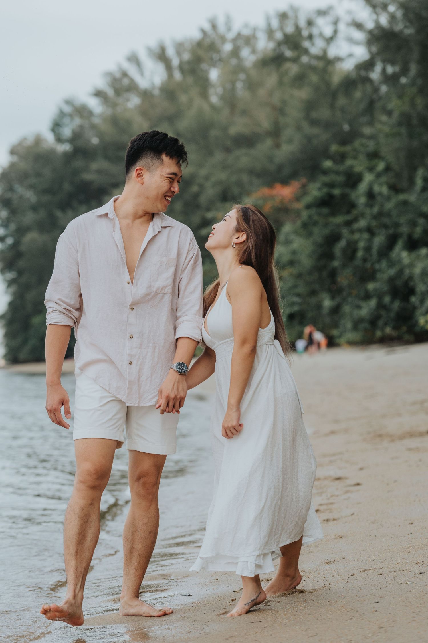 A couple shares a joyful moment while walking along the water's edge.