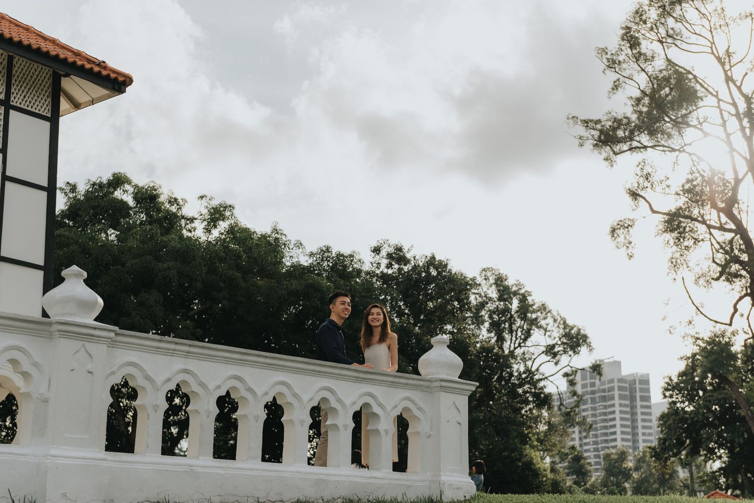 Figures stand on ornate white balcony of colonial building against cloudy sky.