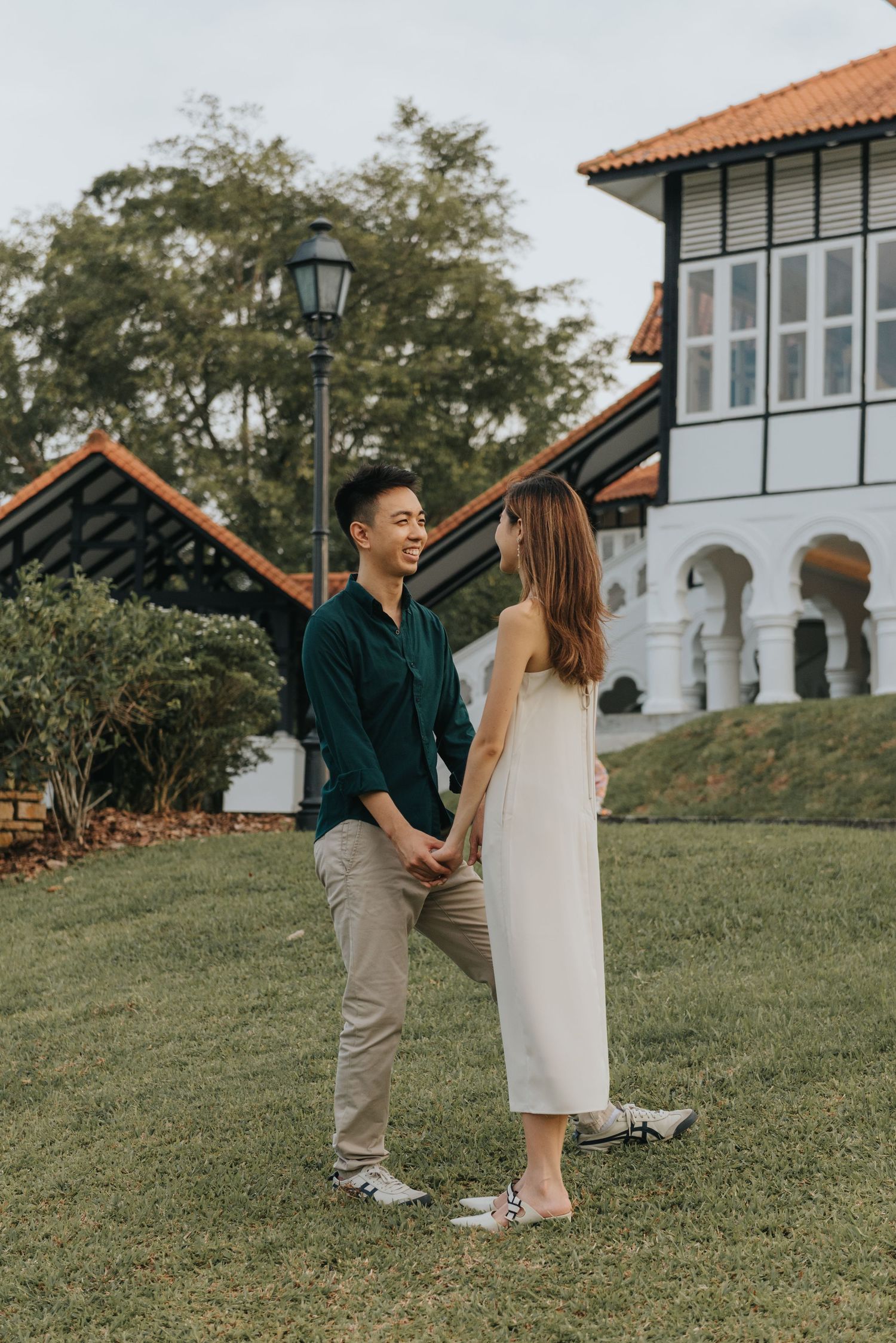 Couple laughing together on a grassy hill with white colonial building in background.