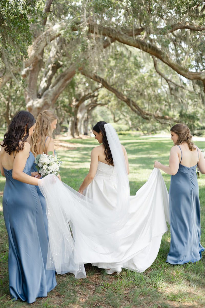 Bridesmaids carrying the bride’s train under the Avenue of Oaks. Sea Island–St. Simons Island wedding in Georgia.