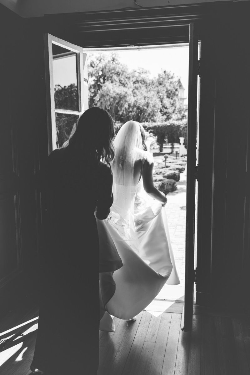 Candid editorial image of bridesmaid carrying the bride’s train at Crane Cottage, Jekyll Island Club Resort, captured by photographer.