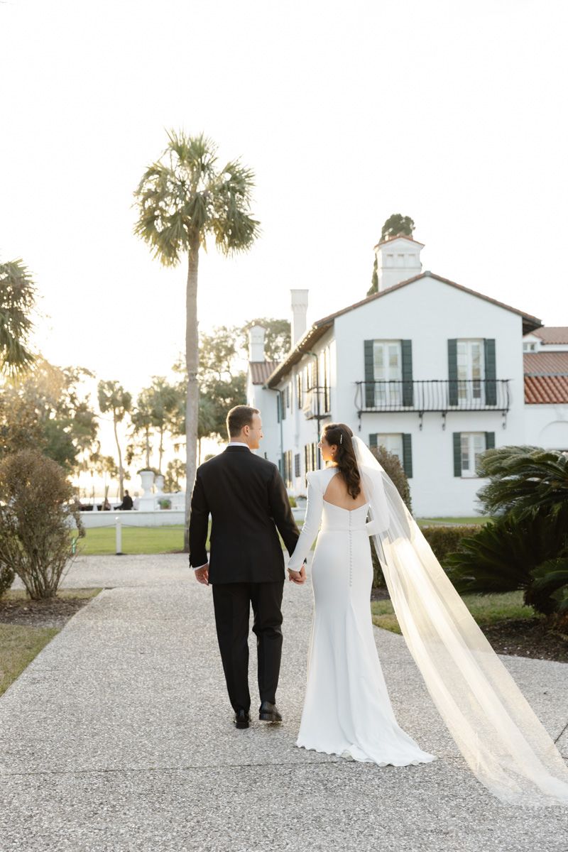 Bride and groom walking with Crane Cottage in the background at Jekyll Island in the Golden Isles, captured by a wedding photographer.