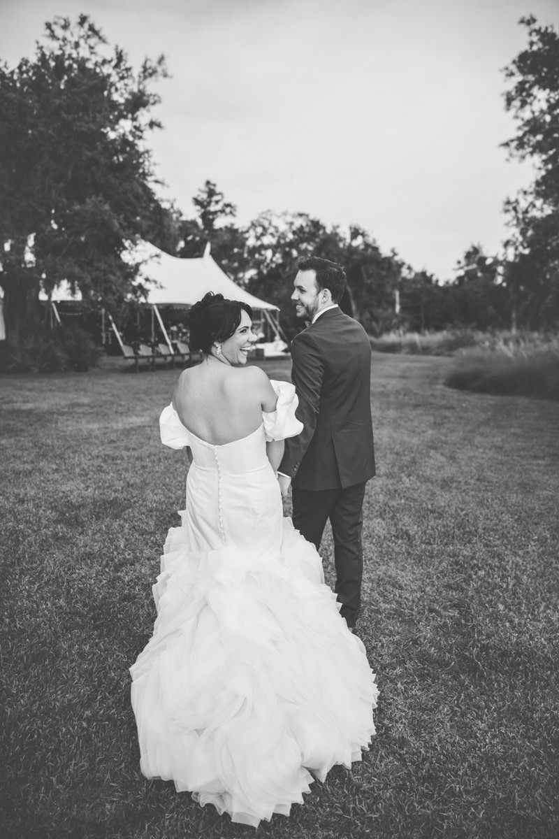 Editorial black-and-white candid of bride and groom entering tented reception at Captain Bluff on St. Simons, with their photographer.